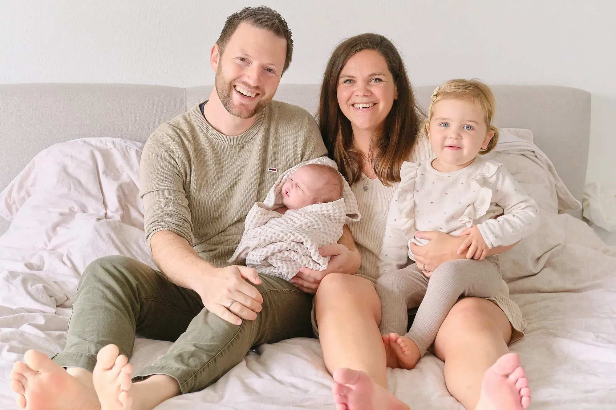 Ouders zitten met hun baby en dochtertje samen op bed