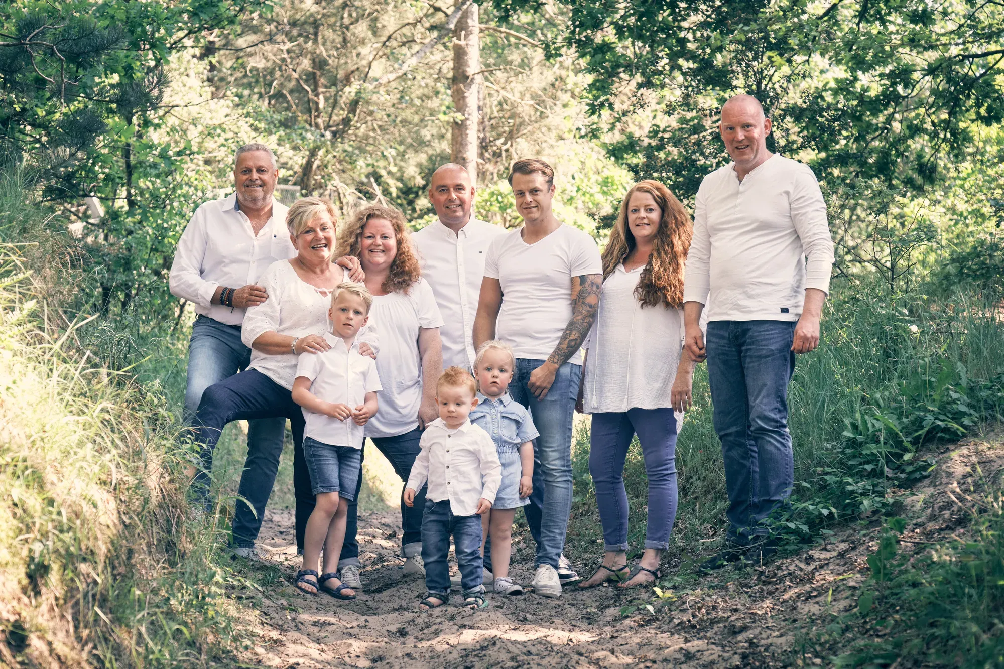 Familie van drie generaties staat lachend samen op een schaduwrijk pad in de duinen