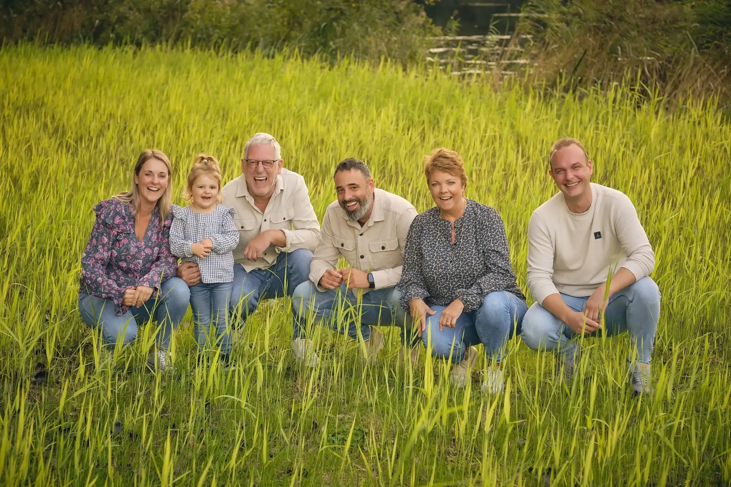 Gezin met vier volwassenen en een kind die glimlachen en poseren in een groene omgeving in Zoetermeer.