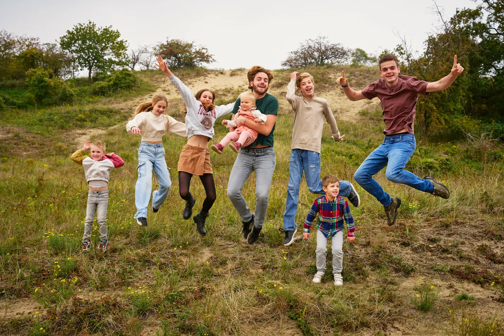 Familie springt tegelijk de lucht in op een begroeide duinhelling