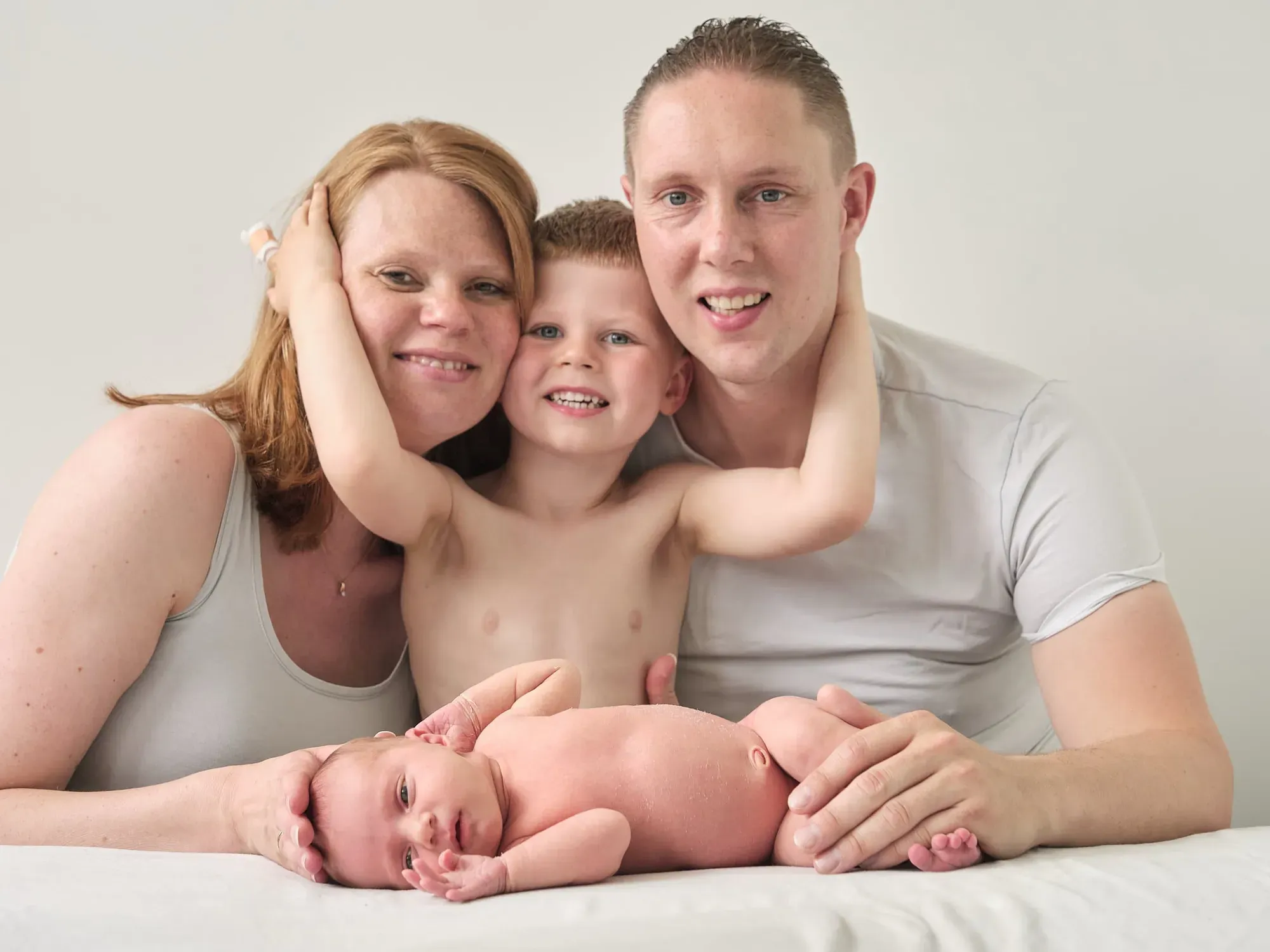 Ouders en grote zus liggen lachend rond de baby