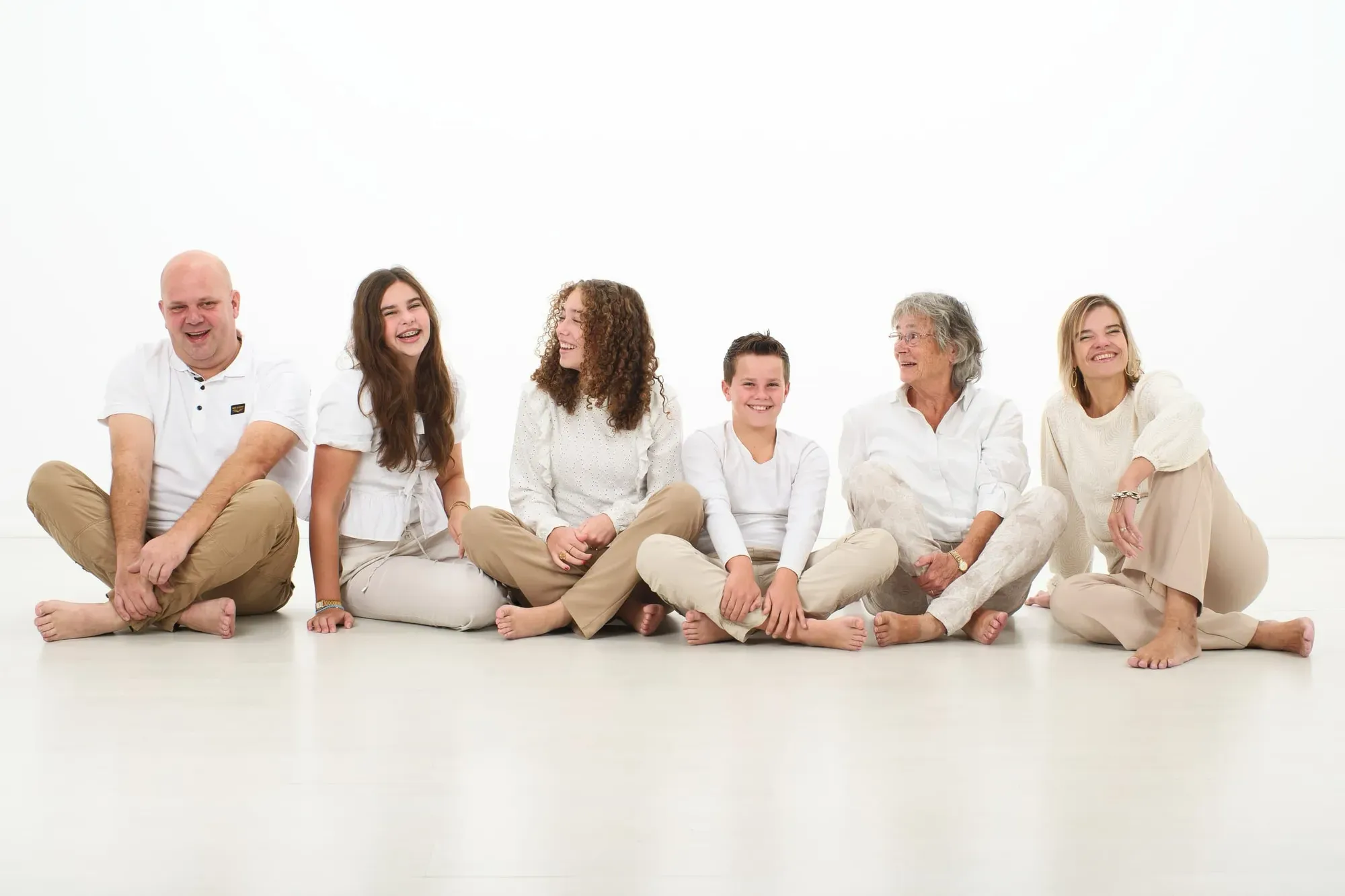 Familie in witte en crèmekleurige kleding zit samen op de vloer van de studio