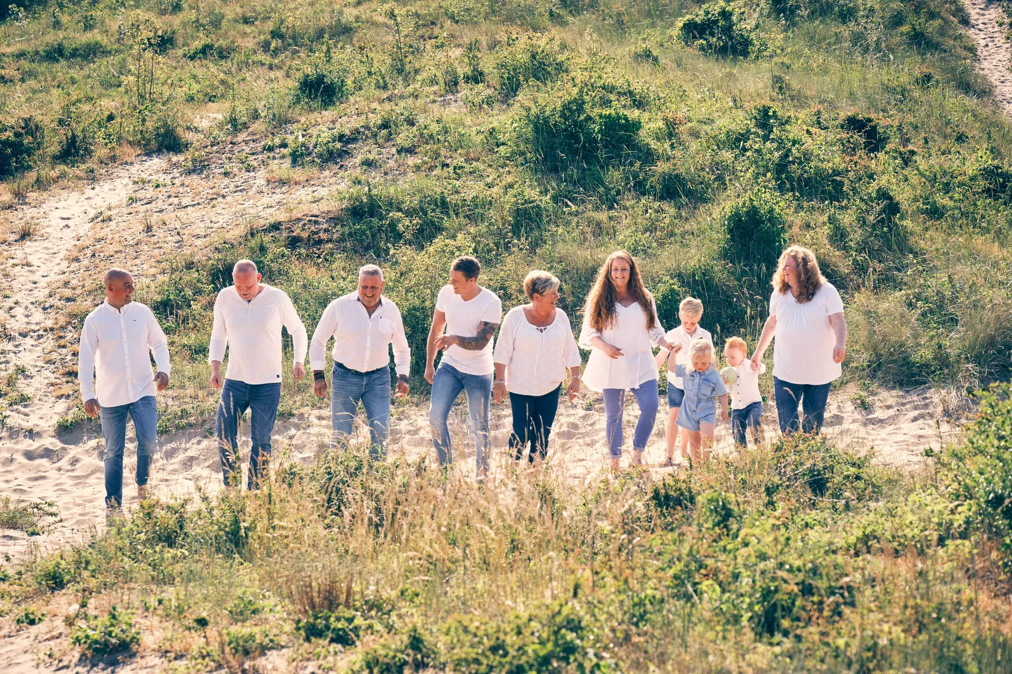 Grote familie loopt hand in hand een duin af