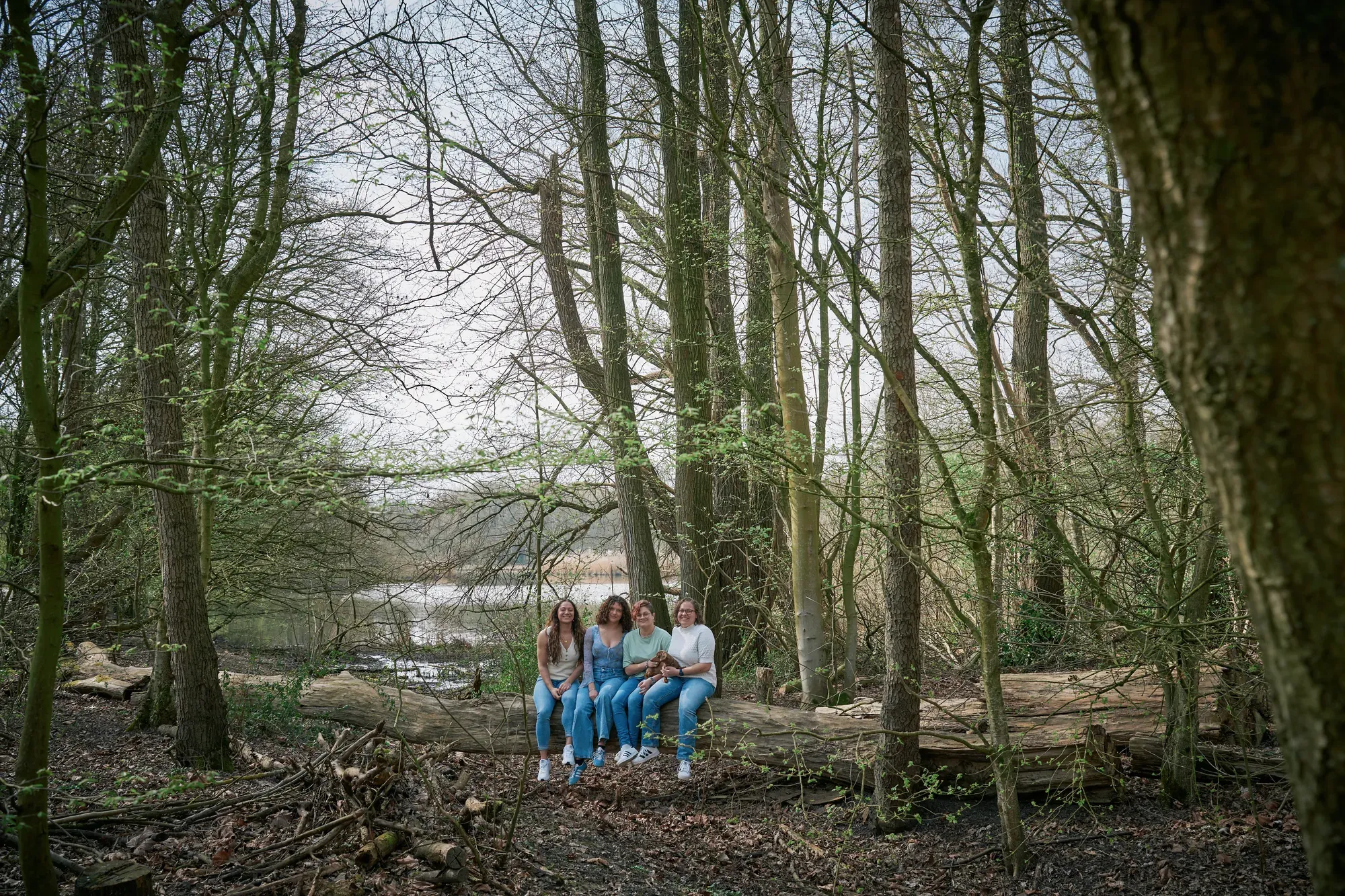 Vier jonge vrouwen zitten op een omgevallen boomstam tussen de kale bomen in het Westerpark