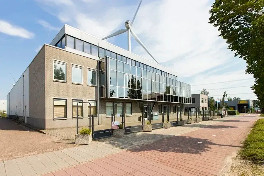 Modern gebouw met veel glas en een windmolen op het dak, gelegen in een commerciële omgeving met een brede voetgangersroute.