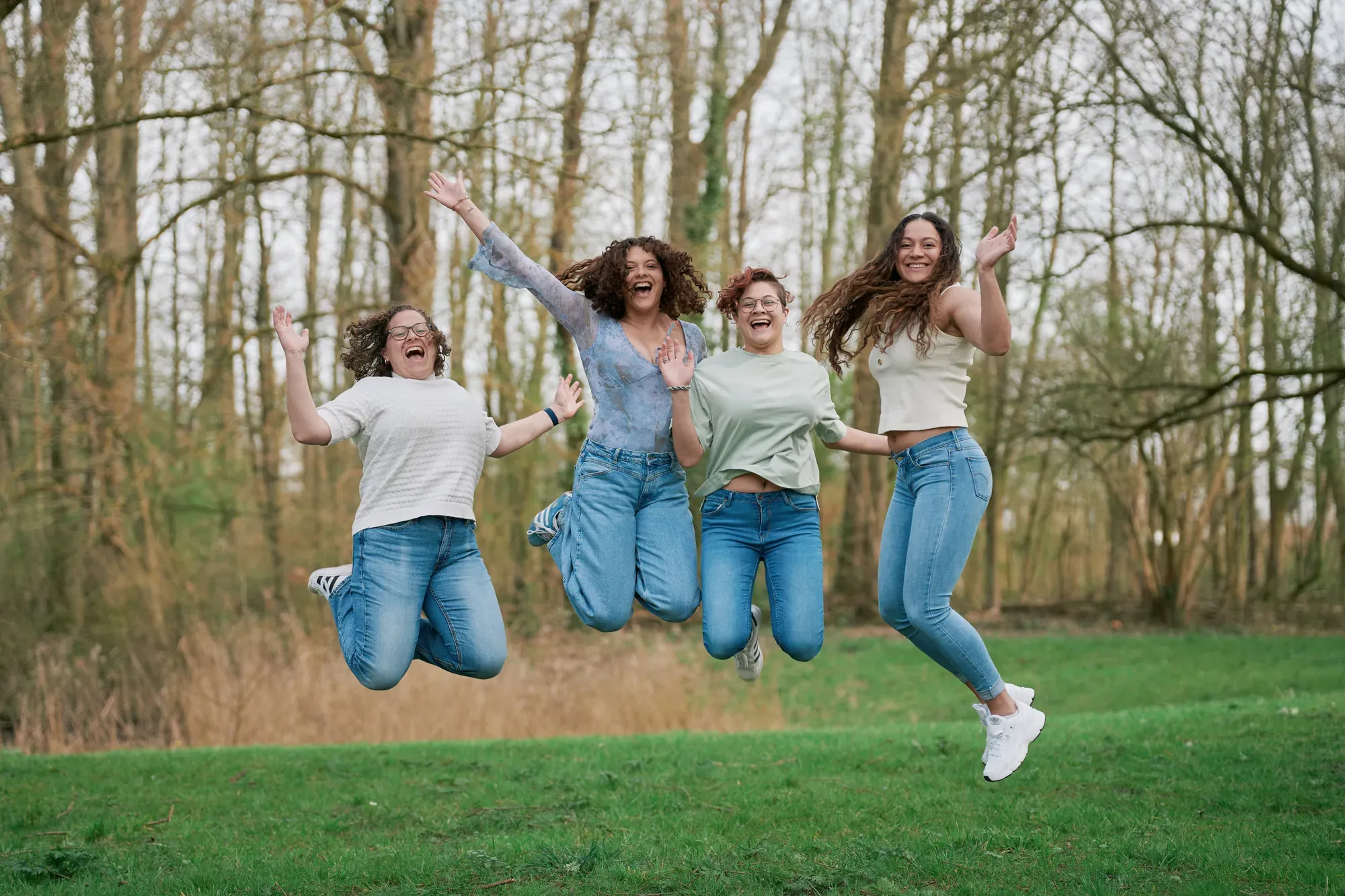 Vier jonge vrouwen springen tegelijk de lucht in op een grasveld in het Westerpark