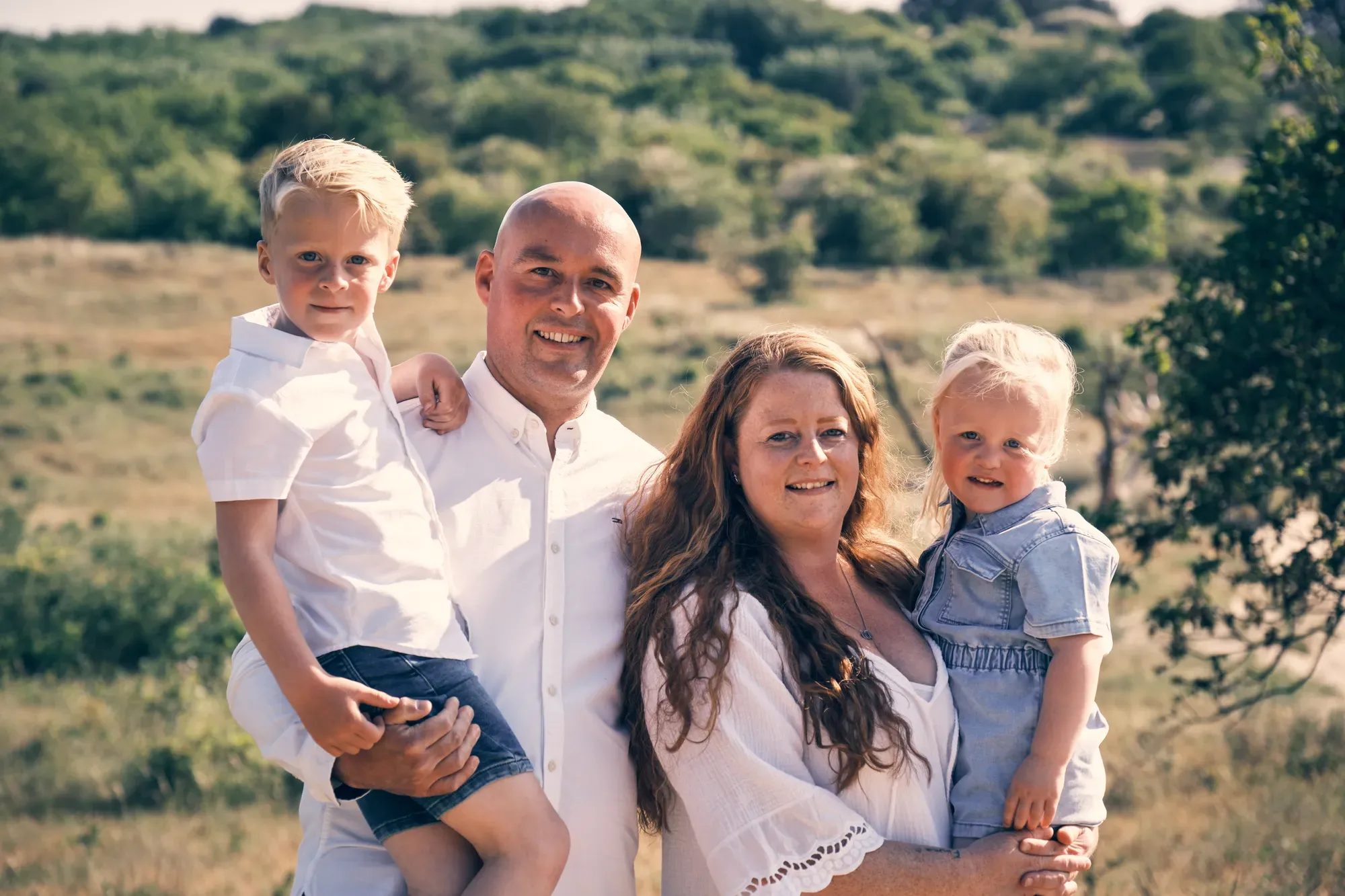 Ouders knuffelen met hun twee jonge kinderen in de duinen bij tegenlicht
