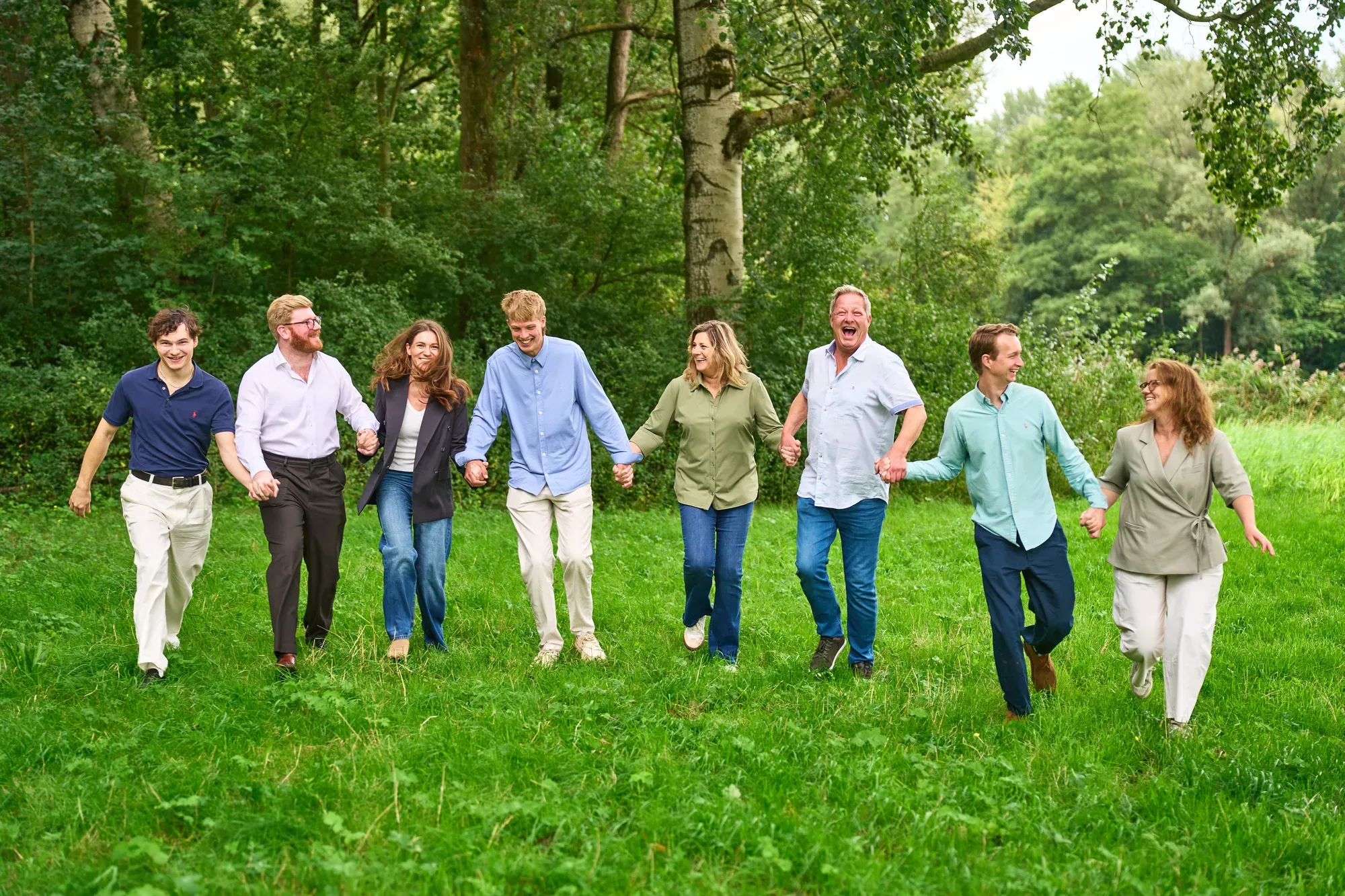 Familie loopt hand in hand lachend door het gras naar de camera