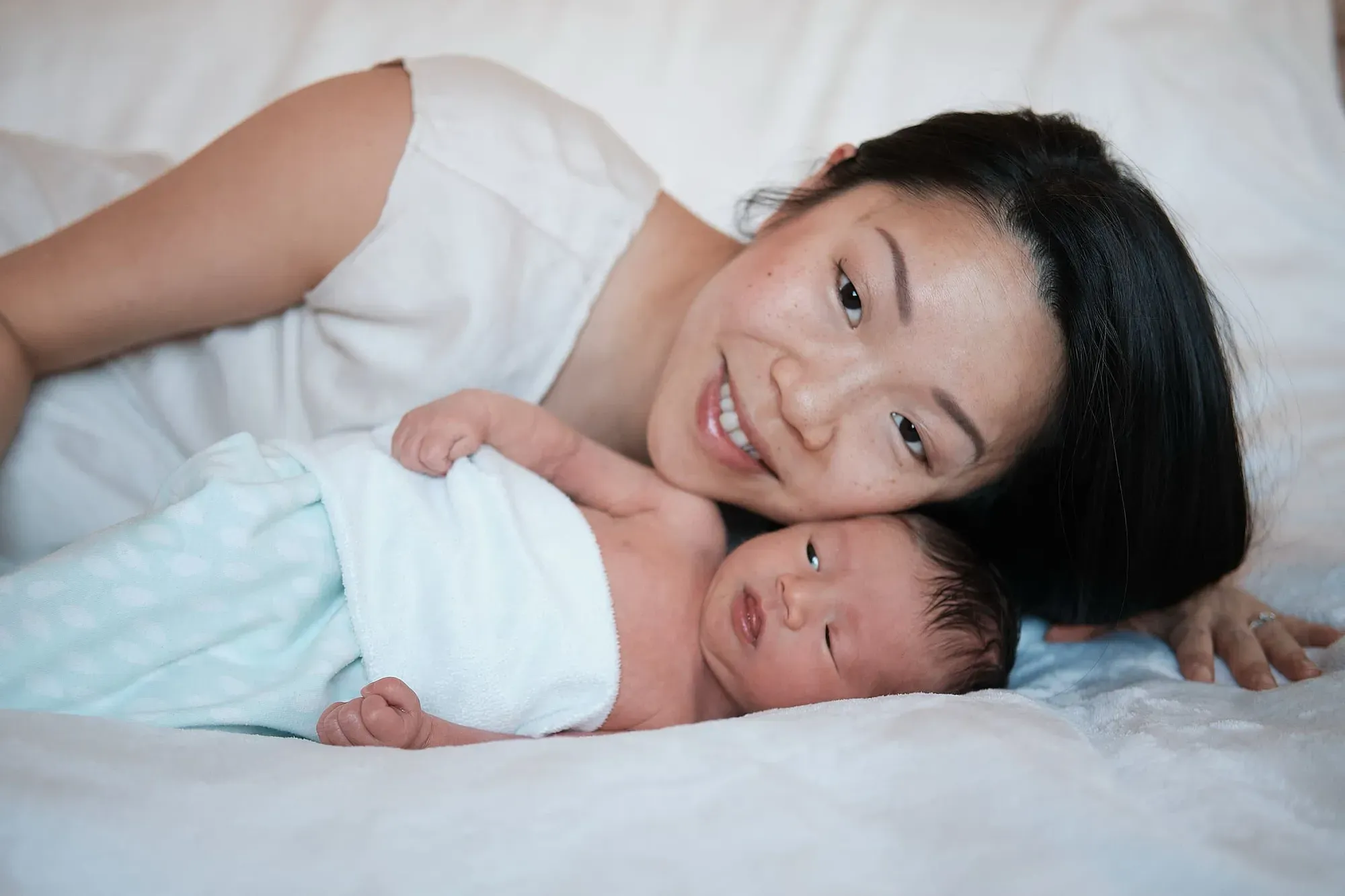Moeder ligt op bed naast haar baby en kijkt naar haar kindje