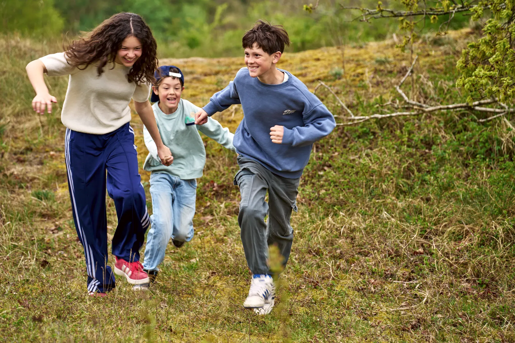 Drie kinderen rennen lachend over het gras in de duinen