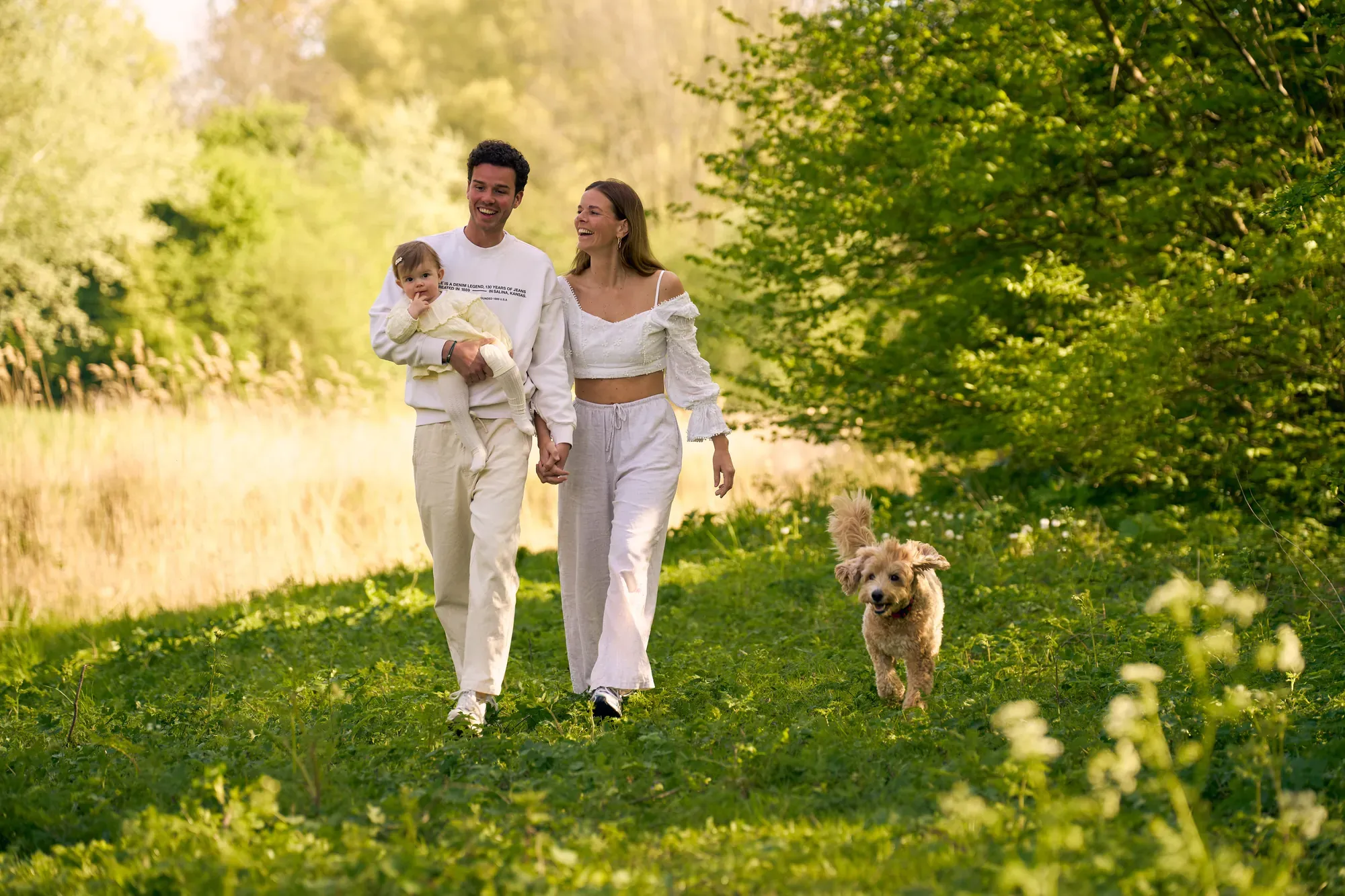 Ouders lopen met hun zoontje en hond over het gras in het lentegroen van het Westerpark