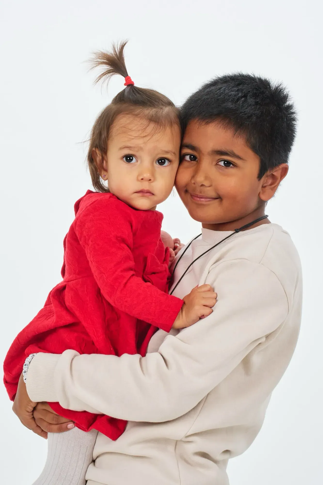 Broer houdt zijn kleine zusje in een rood jurkje lachend vast