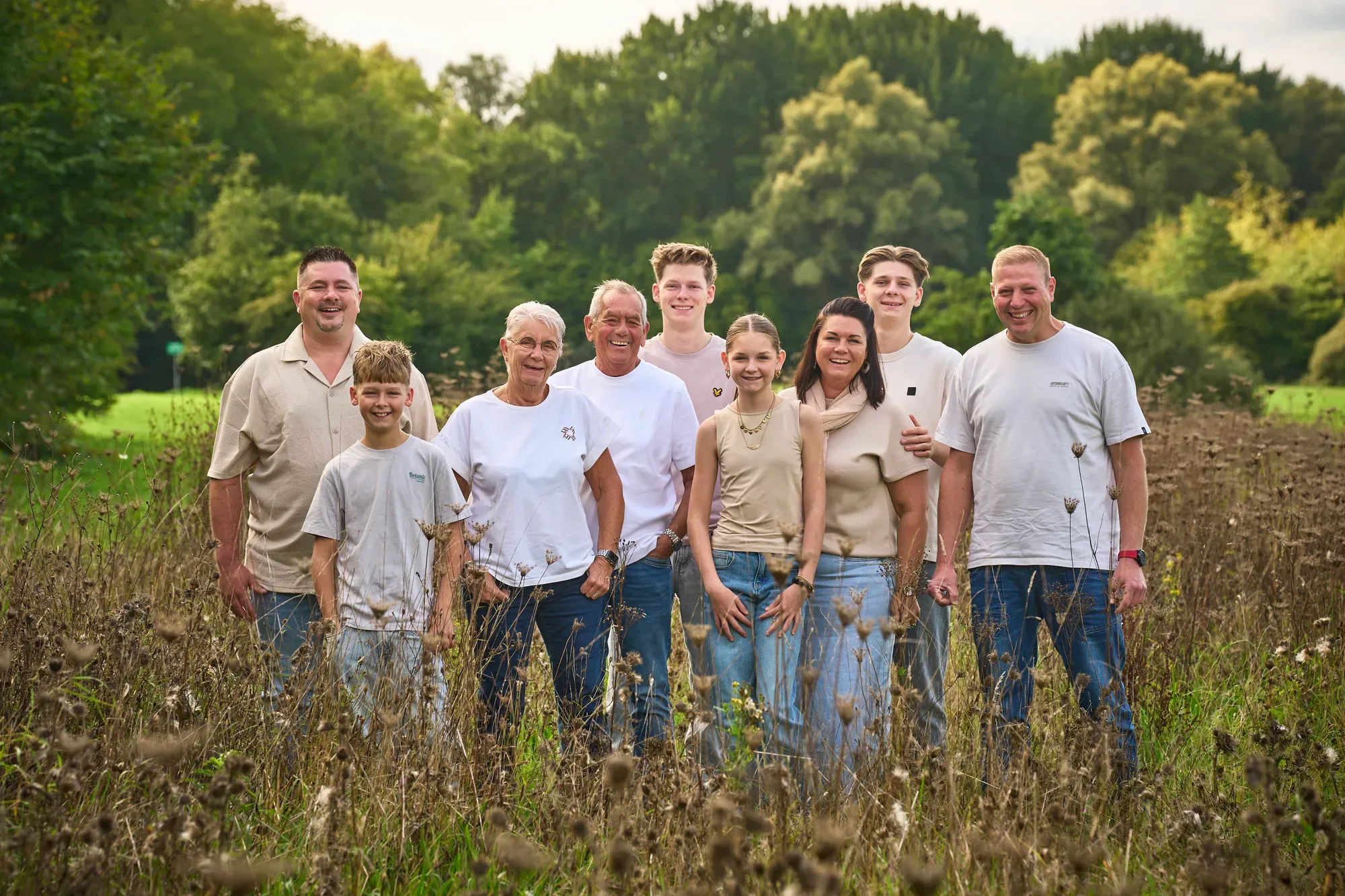 Familie staat samen in het hoge gras met bomen erachter