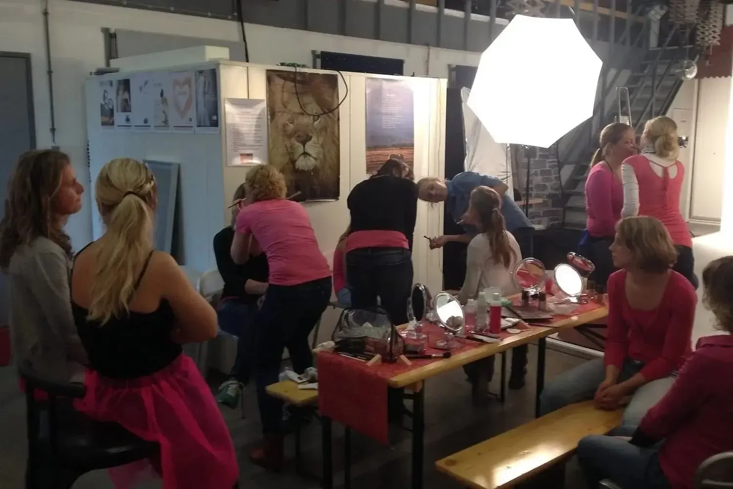 Mensen die zich voorbereiden op een fotoshoot of een make-up sessie in een studio, met verlichte achtergrond en fotografische artistieke decoraties.
