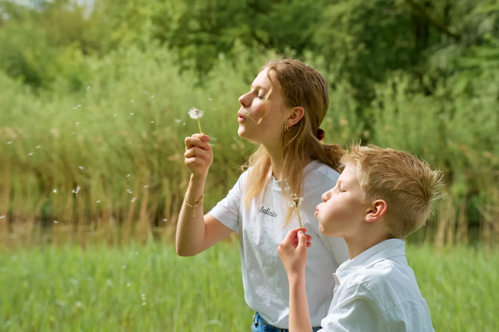 Zus en broer blazen paardenbloemen uit in het gras van het Westerpark