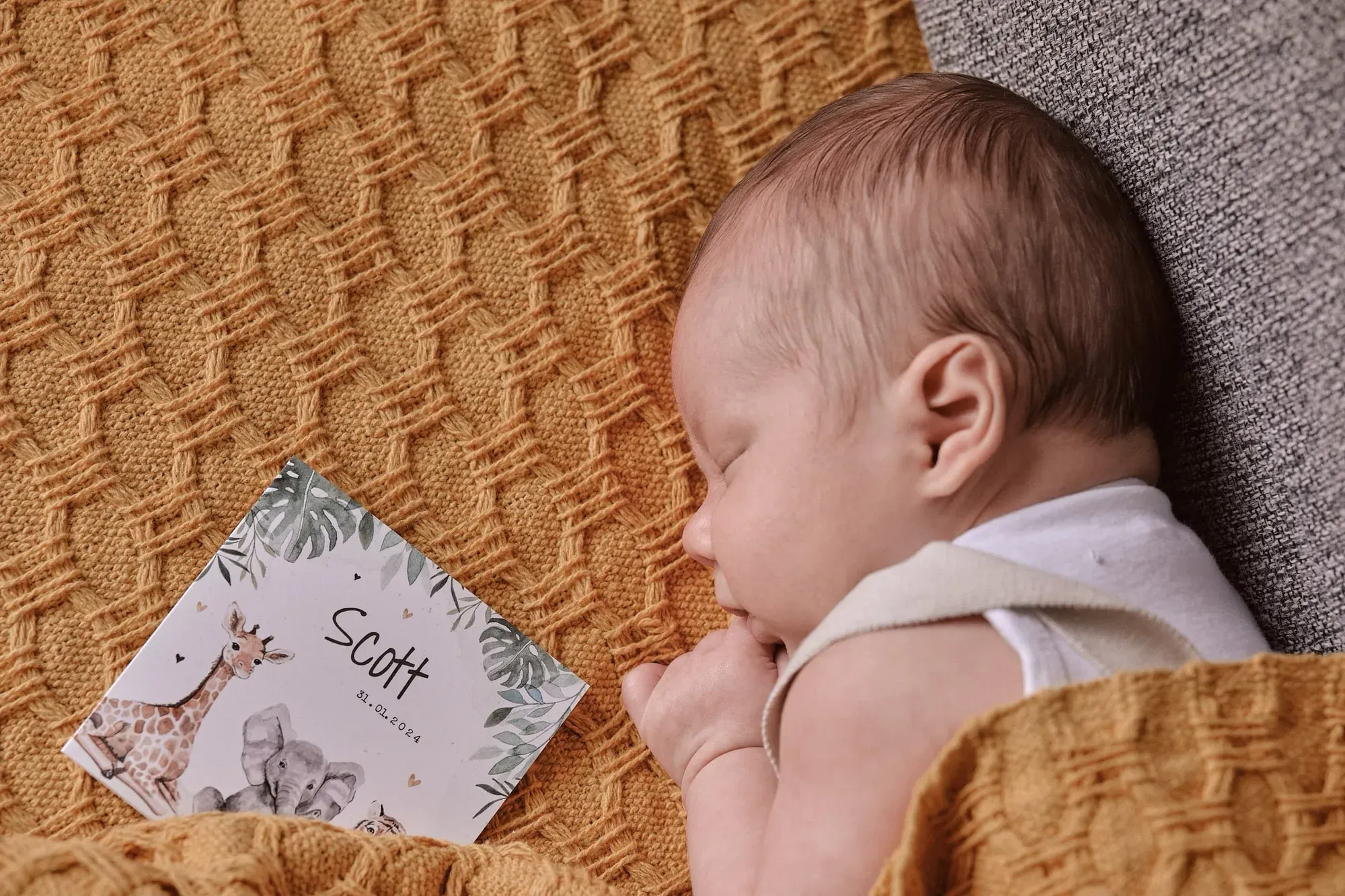 Slapende baby op een oranje deken naast het eigen geboortekaartje