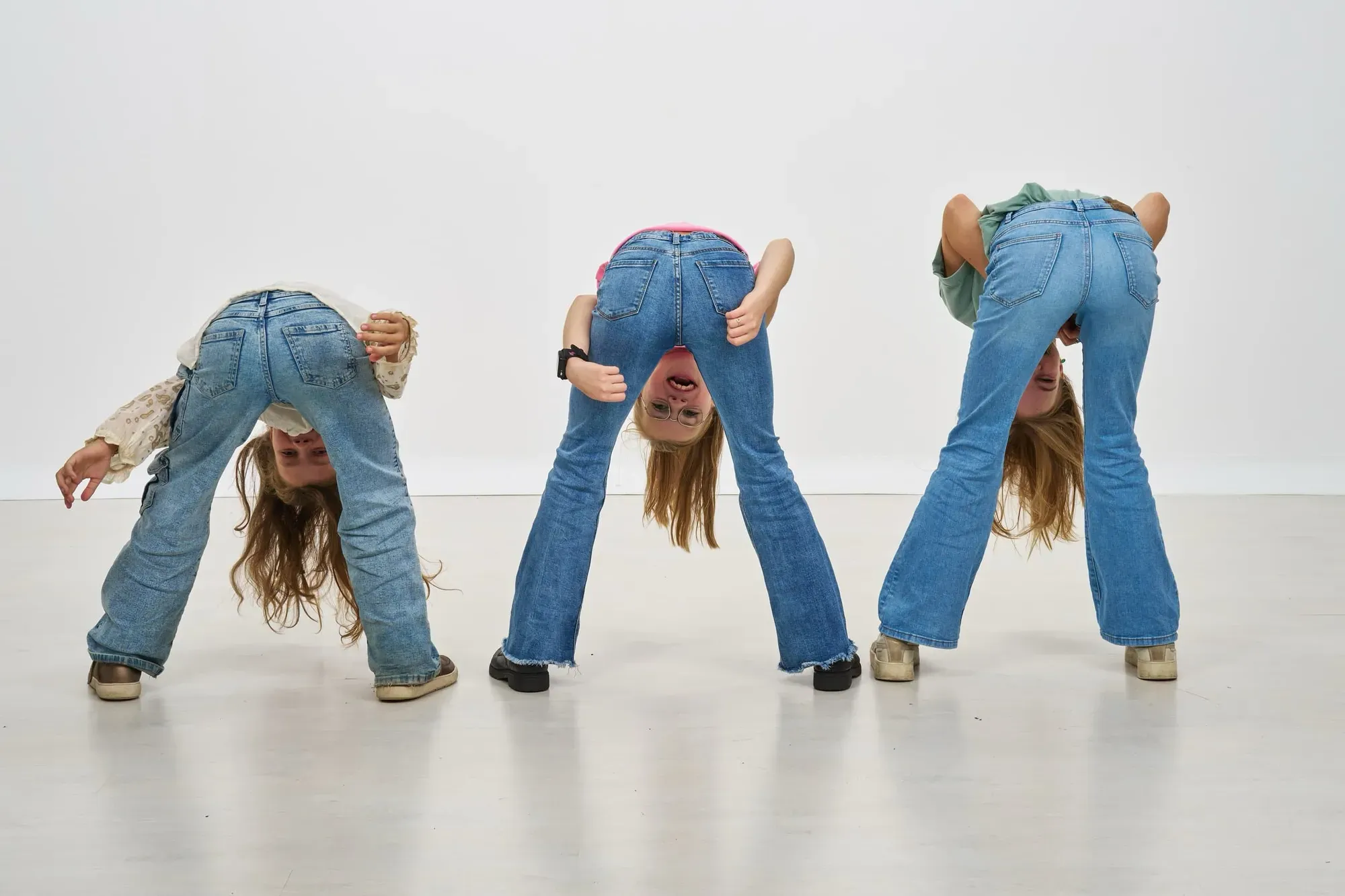 Drie zusjes buigen voorover en kijken ondersteboven tussen hun benen door