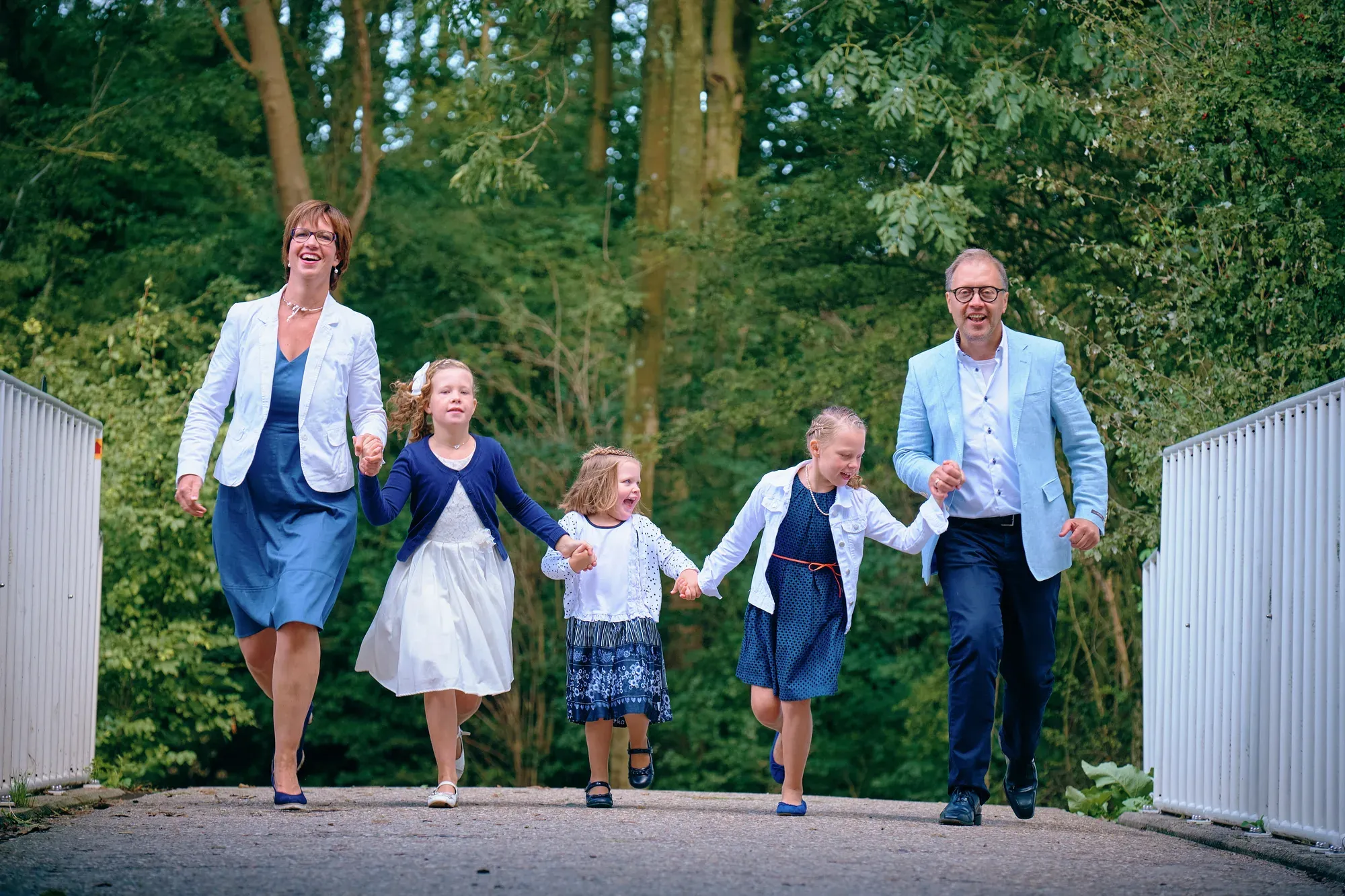 Gezin met drie dochters rent hand in hand over een witte brug in de Delftse Hout