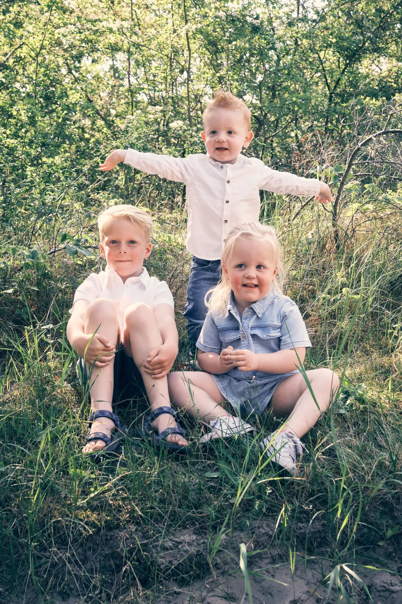 Drie kinderen spelen in het duinzand tussen het helmgras