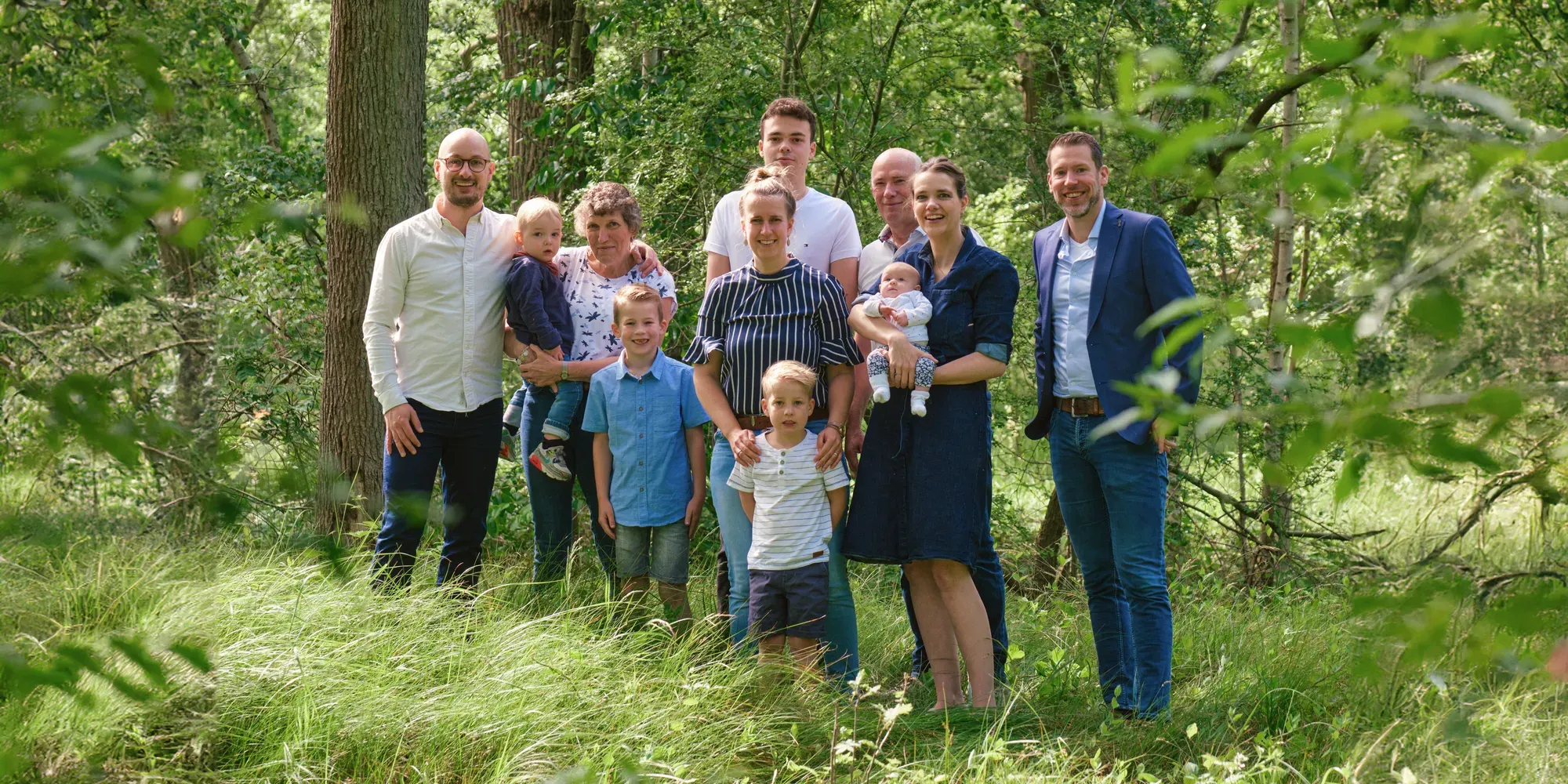 Grote familie met kleine kinderen staat tussen het groen in het bos