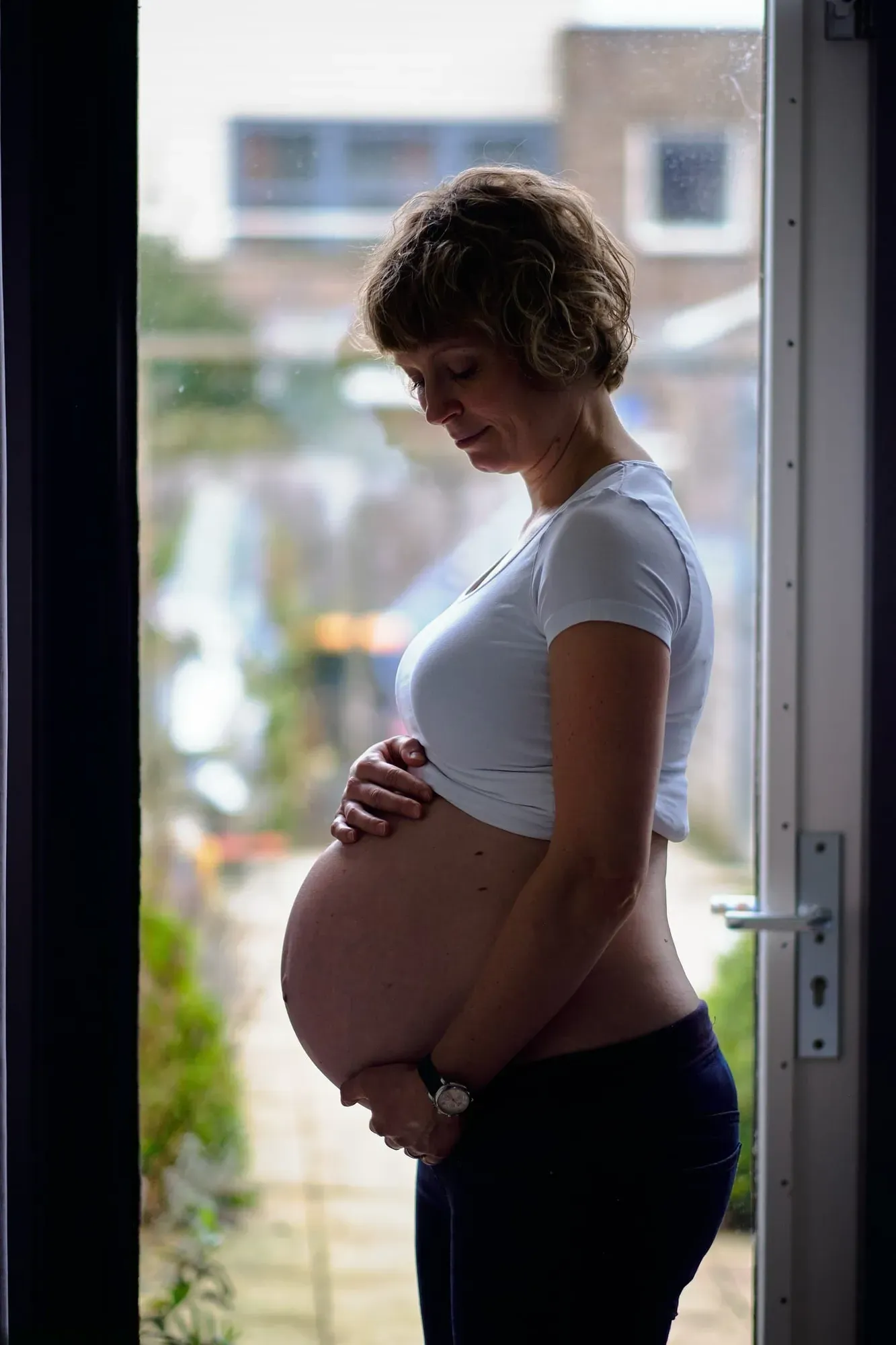 Zwangere vrouw staat thuis bij het raam in zacht daglicht