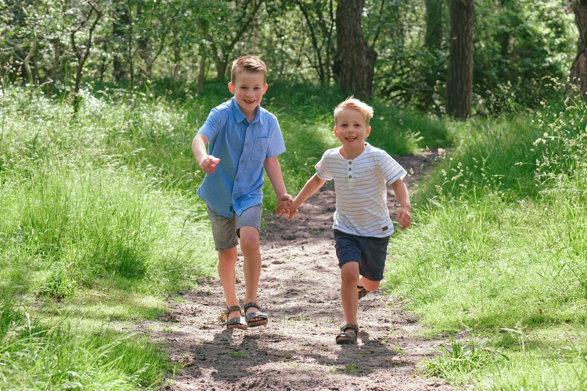 Twee jongens rennen over een smal pad door het hoge gras