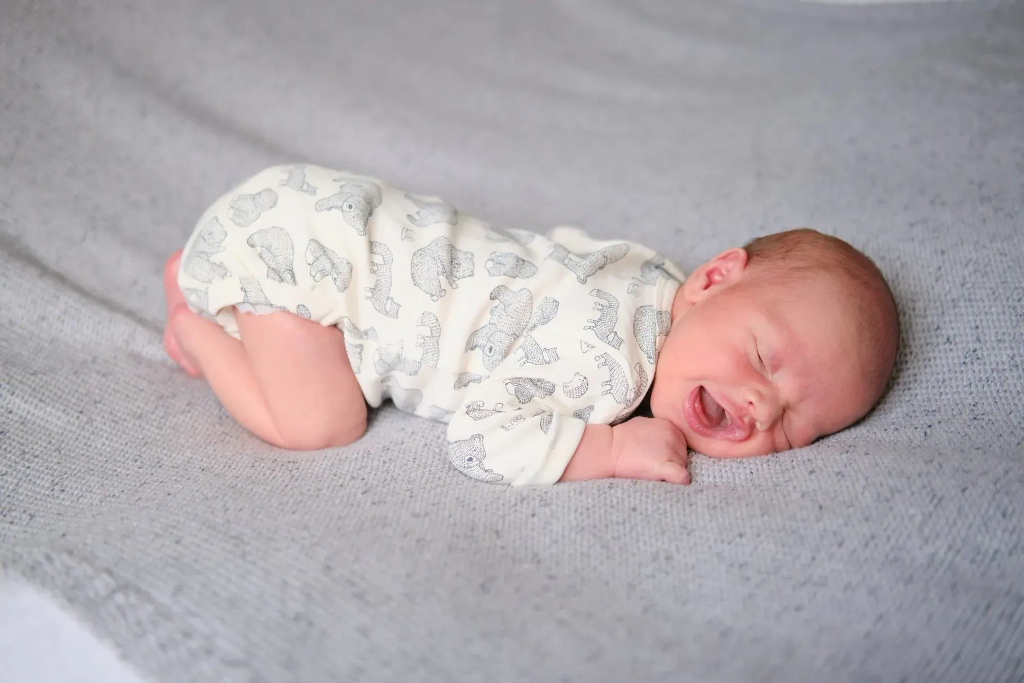Pasgeboren baby slaapt opgerold op een grijze deken