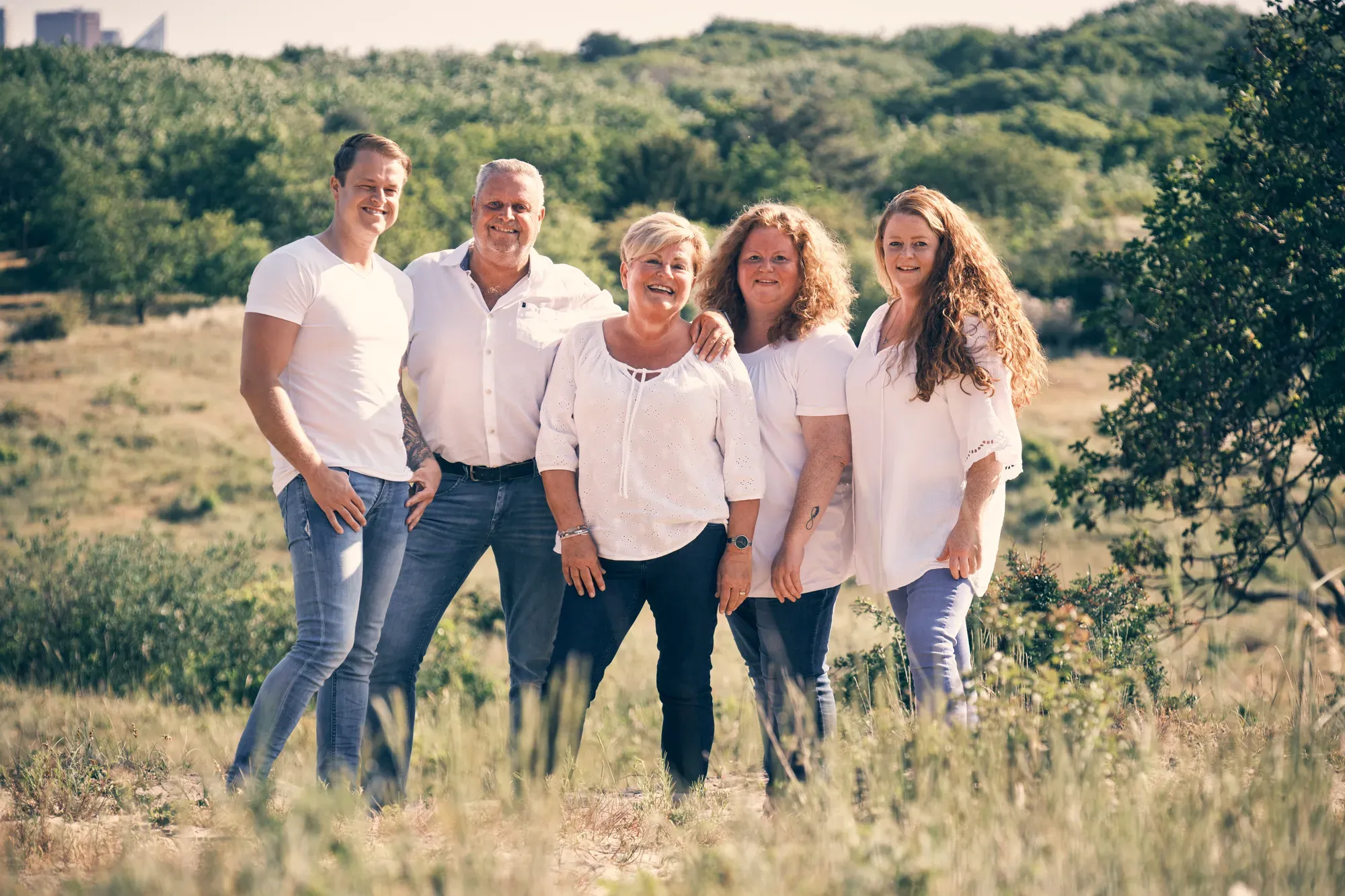 Familie van drie generaties poseert rond een oude, kale boom in de duinen