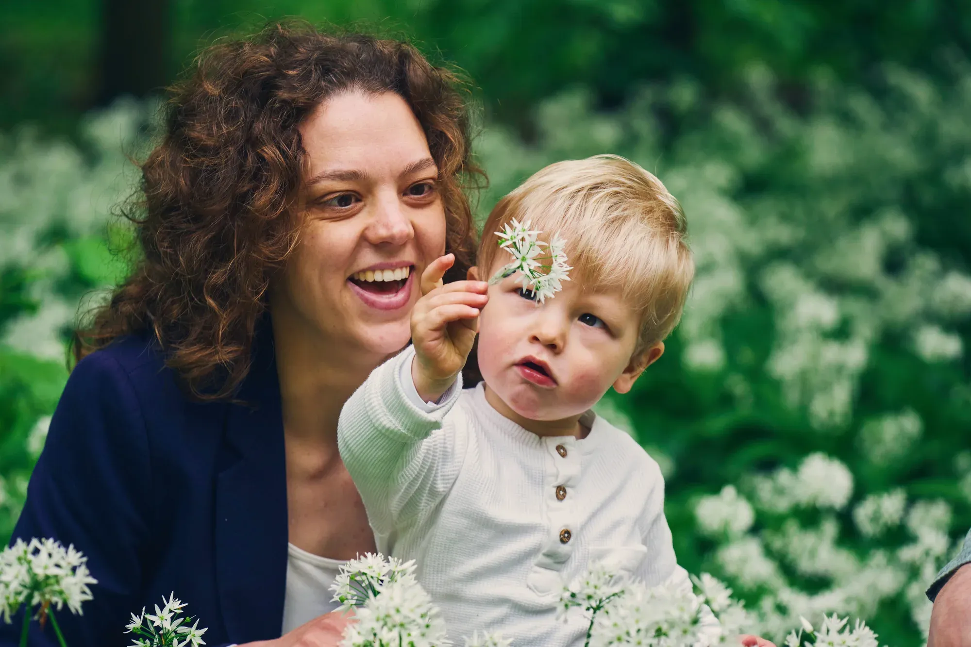 Lachende moeder met zoontje dat een witte daslookbloem vasthoudt