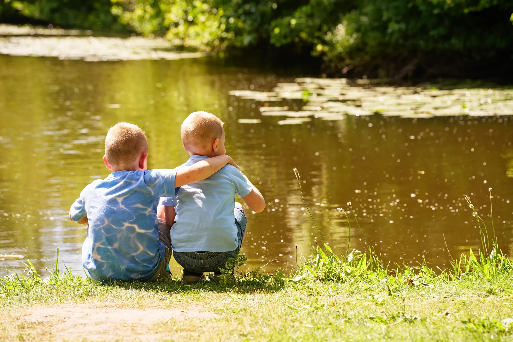 Twee broertjes zitten met hun rug naar de camera aan het water in het Westerpark