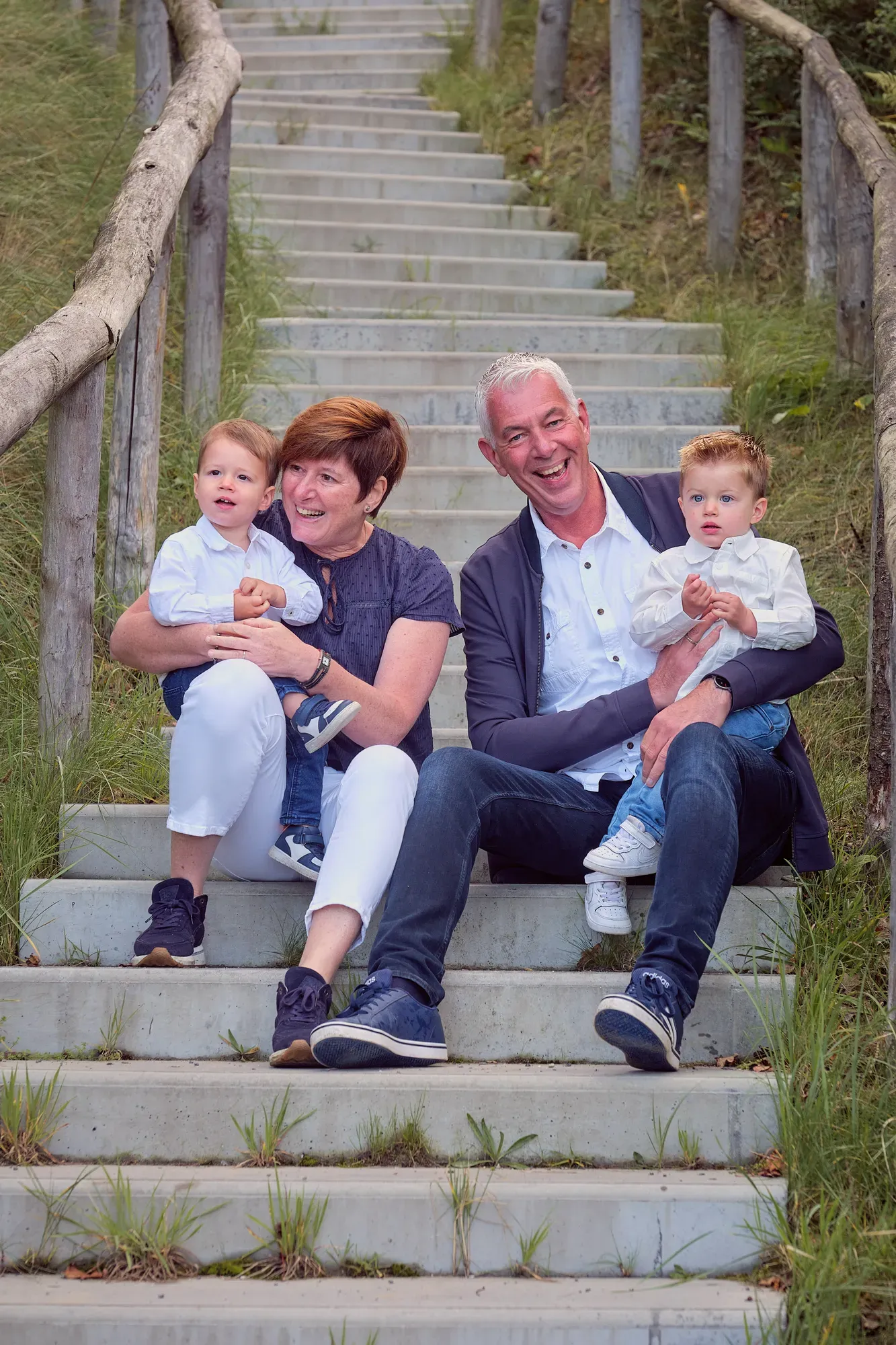 Opa en oma zitten met twee kleine kinderen op een trap in de duinen