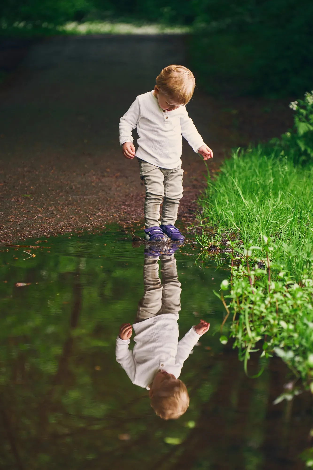 Peuter staat in een plas water en kijkt naar zijn spiegelbeeld