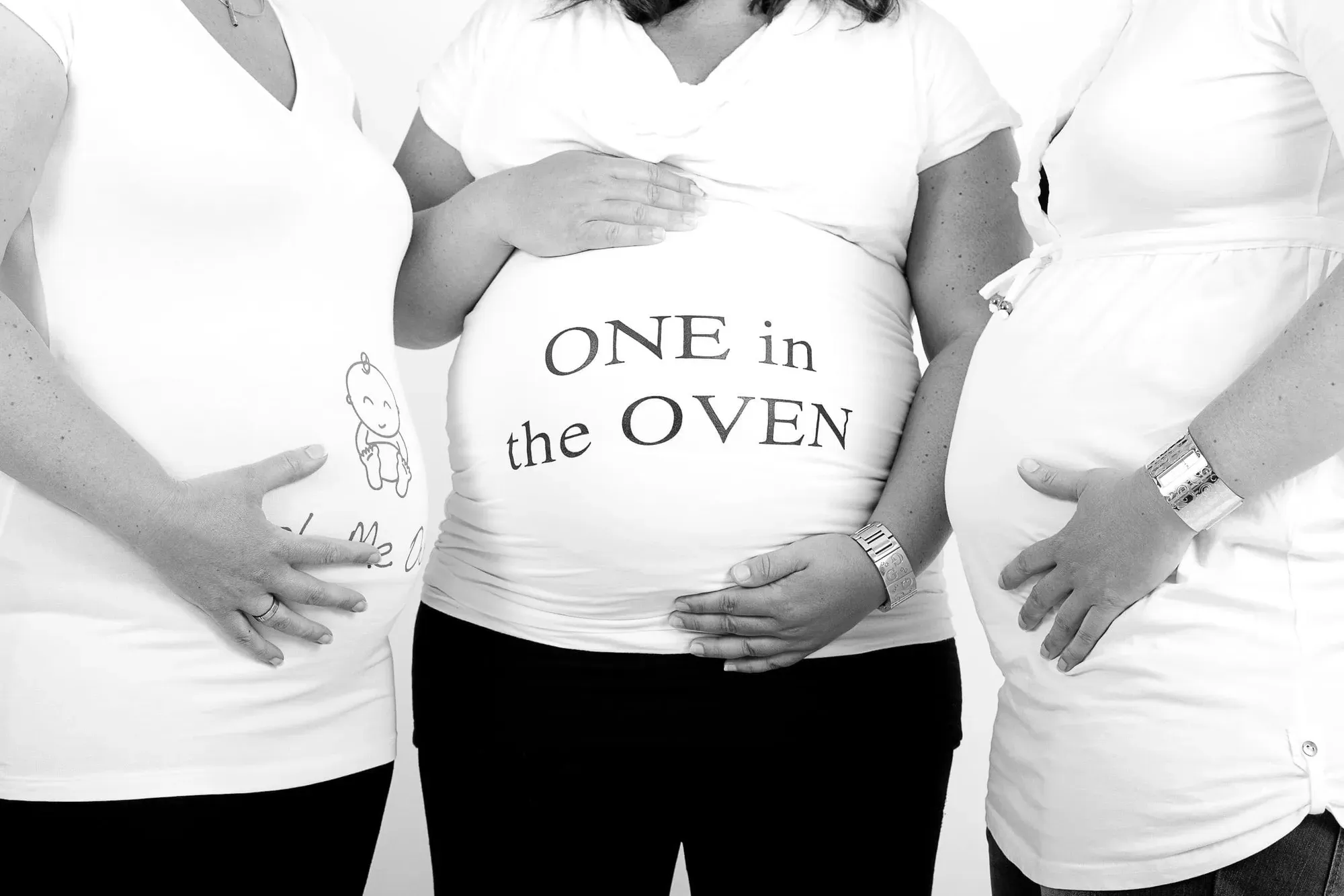 Drie personen in shirts met de tekst one in the oven rond de zwangere buik
