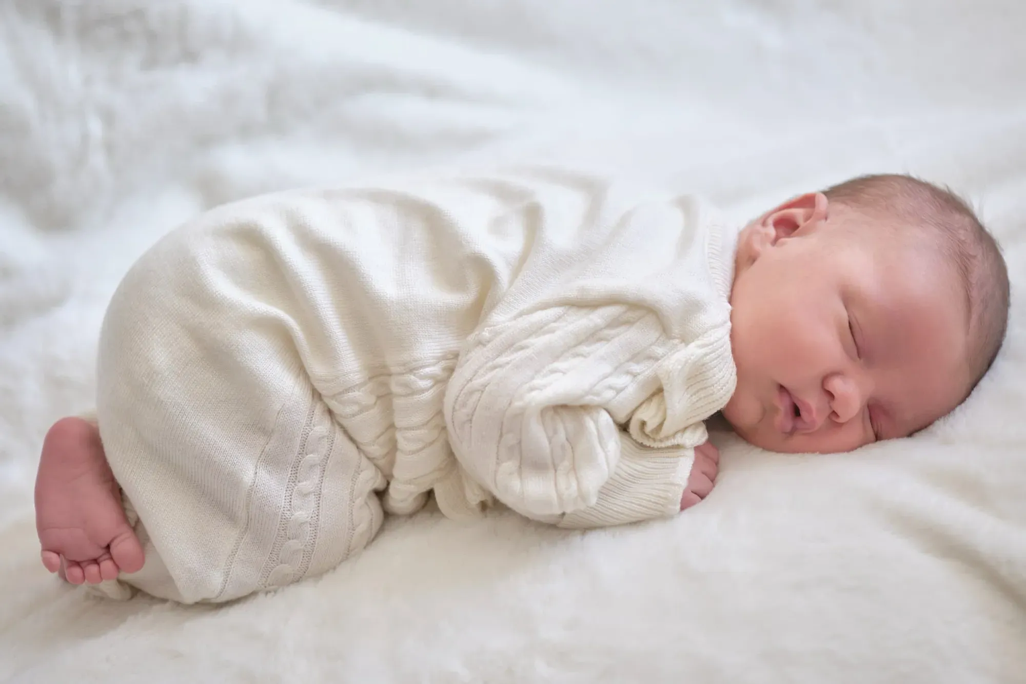 Pasgeboren baby slaapt in een wit pakje op een deken