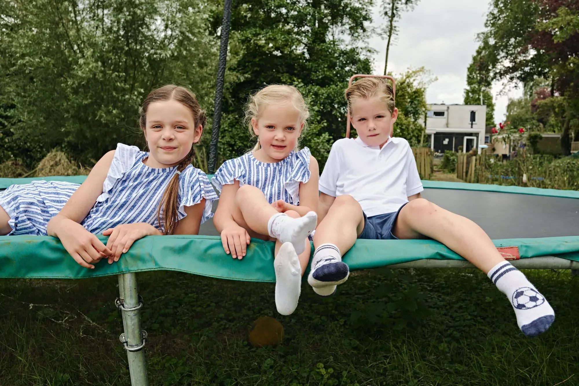 Drie kinderen zitten samen op de trampoline in de tuin