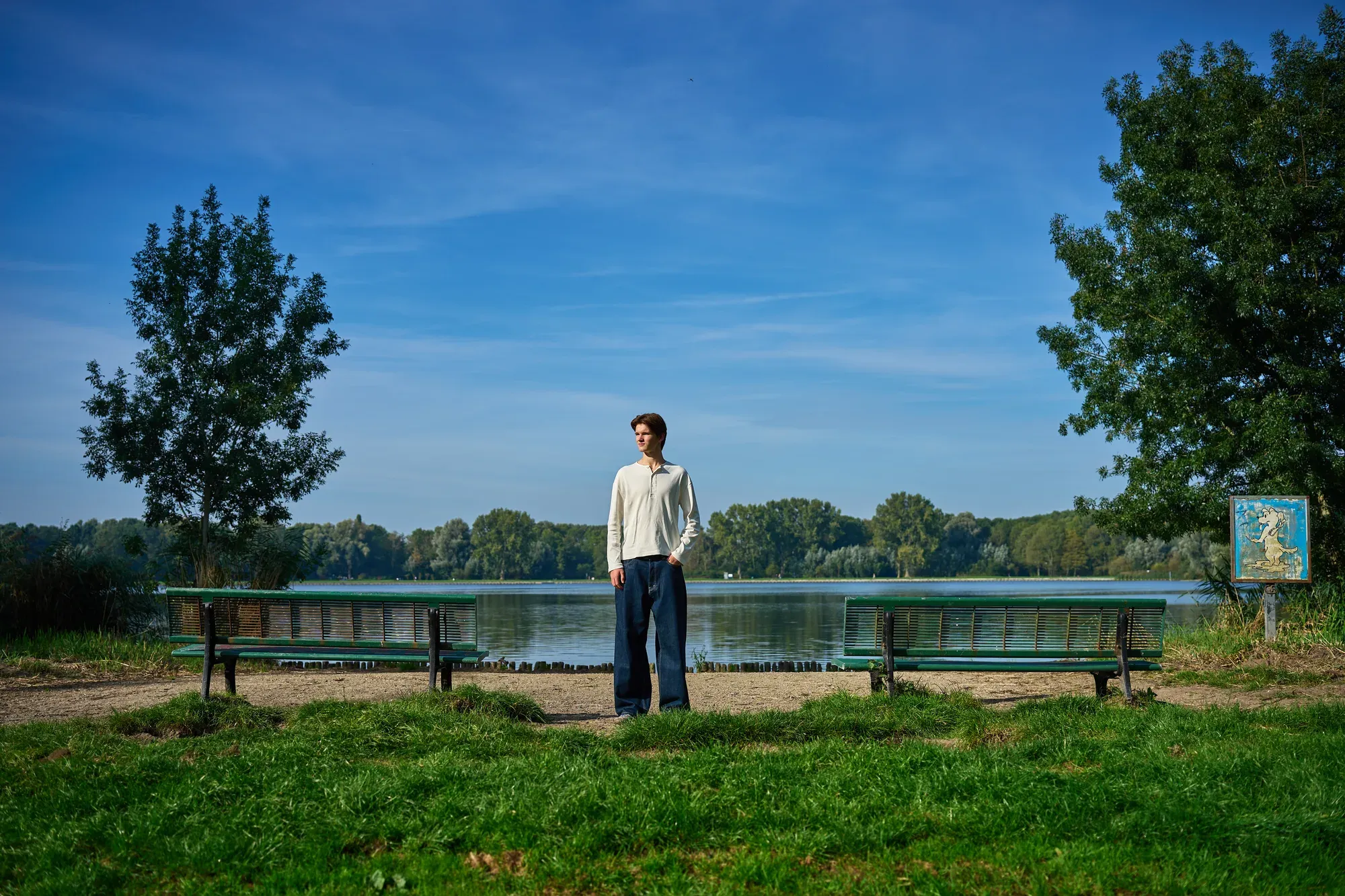 Jongeman staat aan de waterkant in de Delftse Hout, met bankjes en bomen op de achtergrond