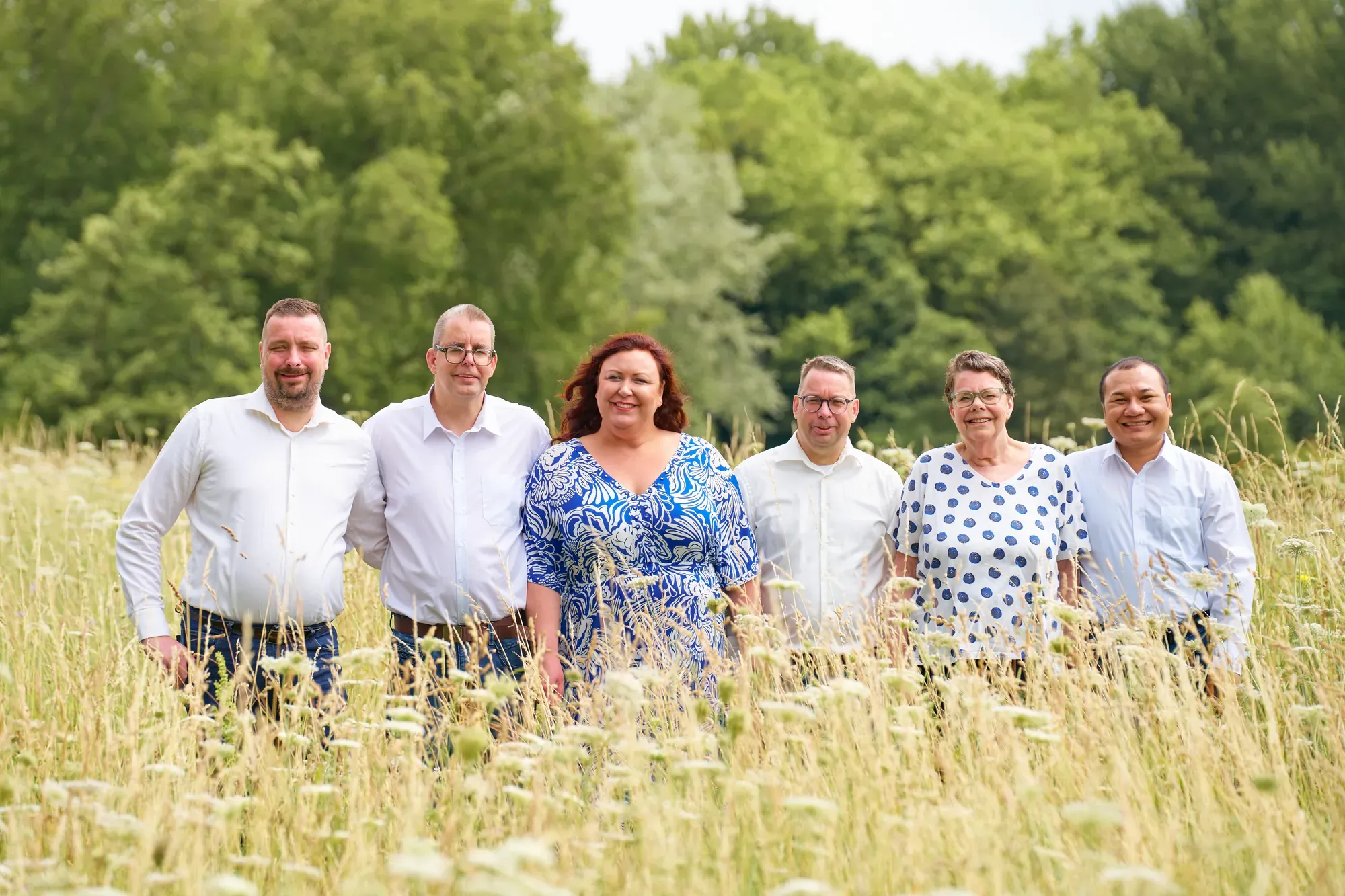 Zes volwassenen staan naast elkaar in het hoge gras van het Westerpark