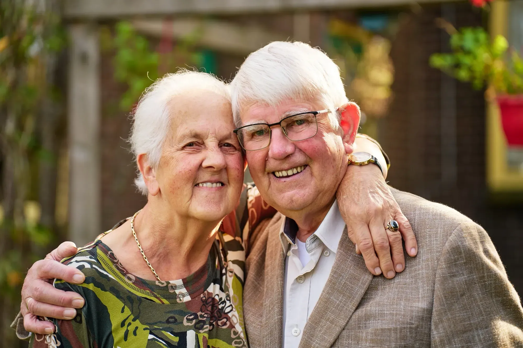 Opa en oma omarmen elkaar lachend in hun tuin