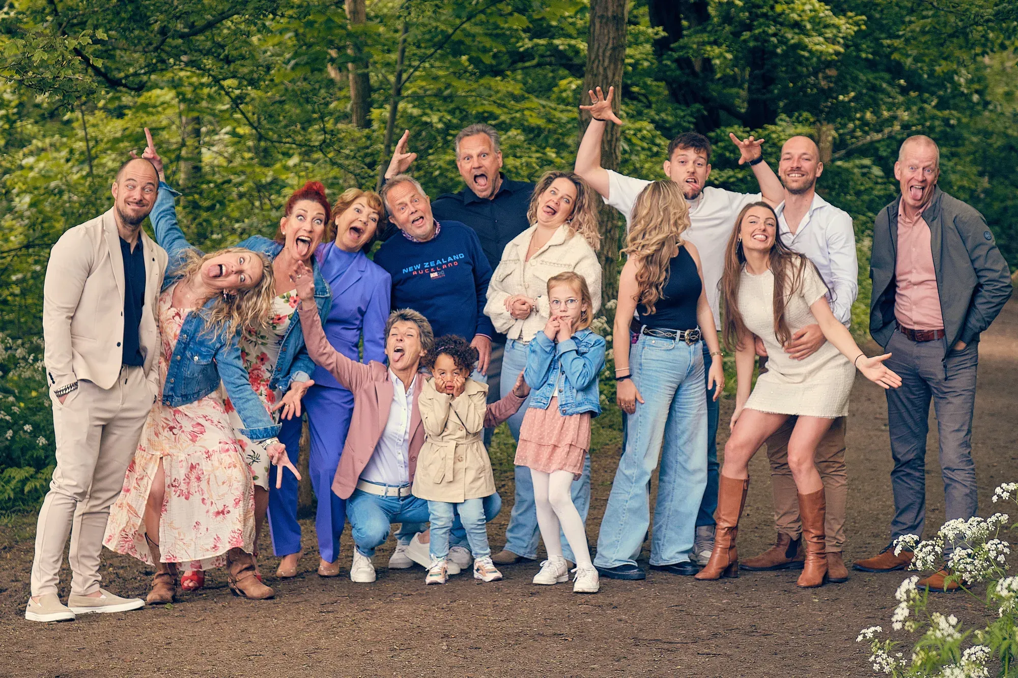Grote familie met drie generaties maakt uitgelaten gebaren op een bospad tussen hoge bomen