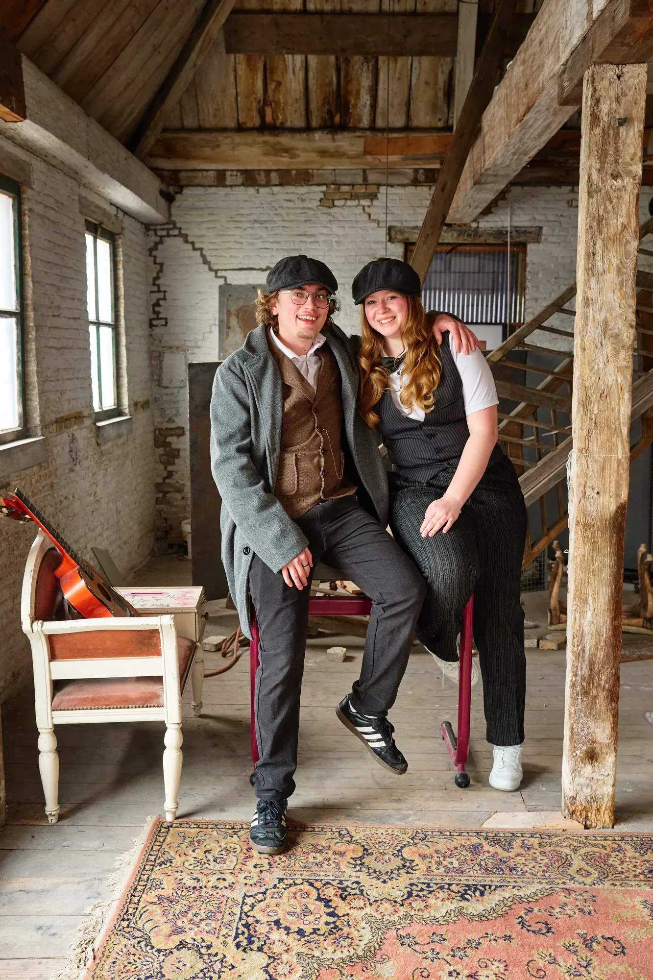 Twee lachende tieners in Peaky Blinders-kleding op oude stoelen
