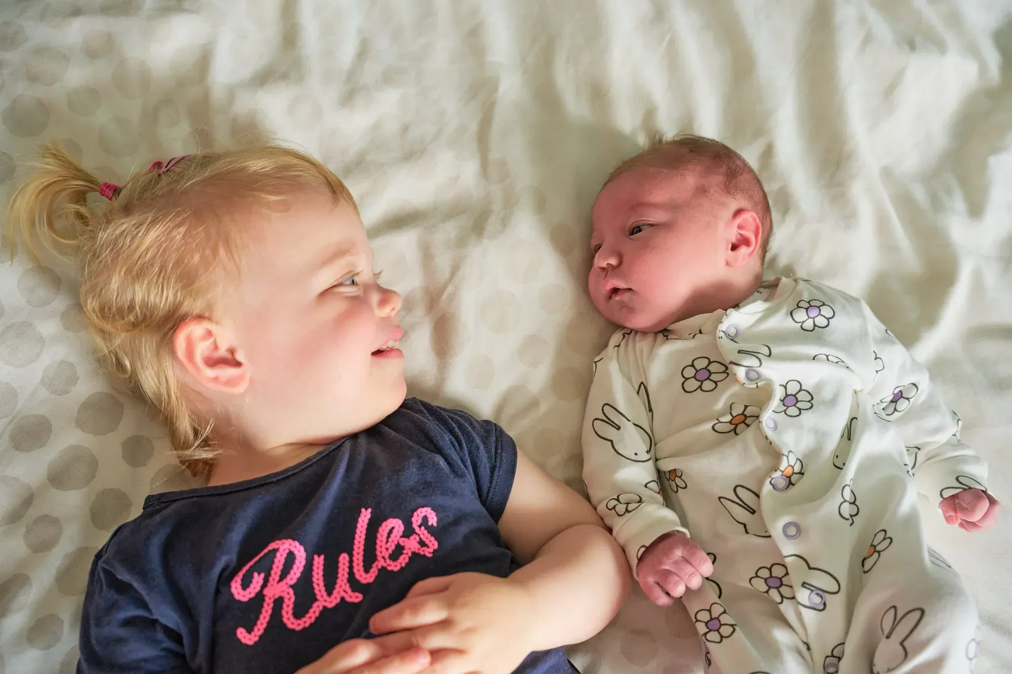 Grote zus ligt op bed en kijkt naar de baby