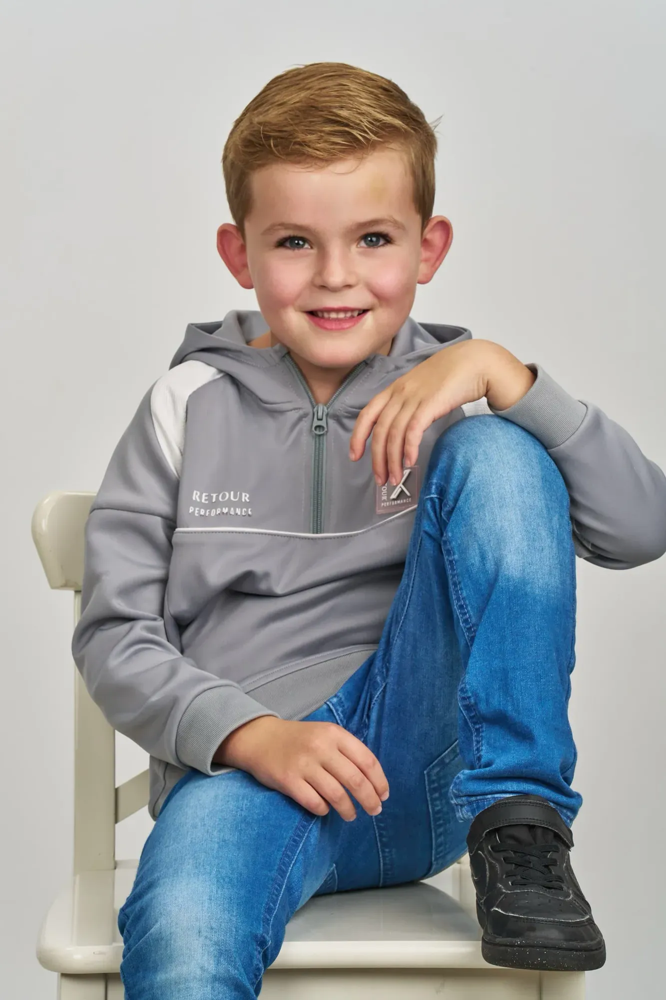 Jongen zit lachend op een houten stoel in de studio