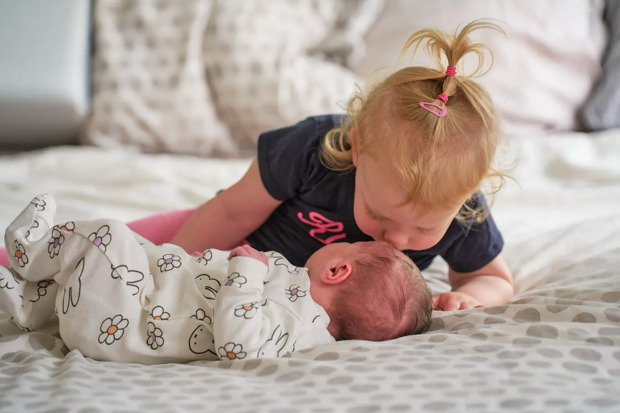 Grote zus geeft de baby een kusje op bed