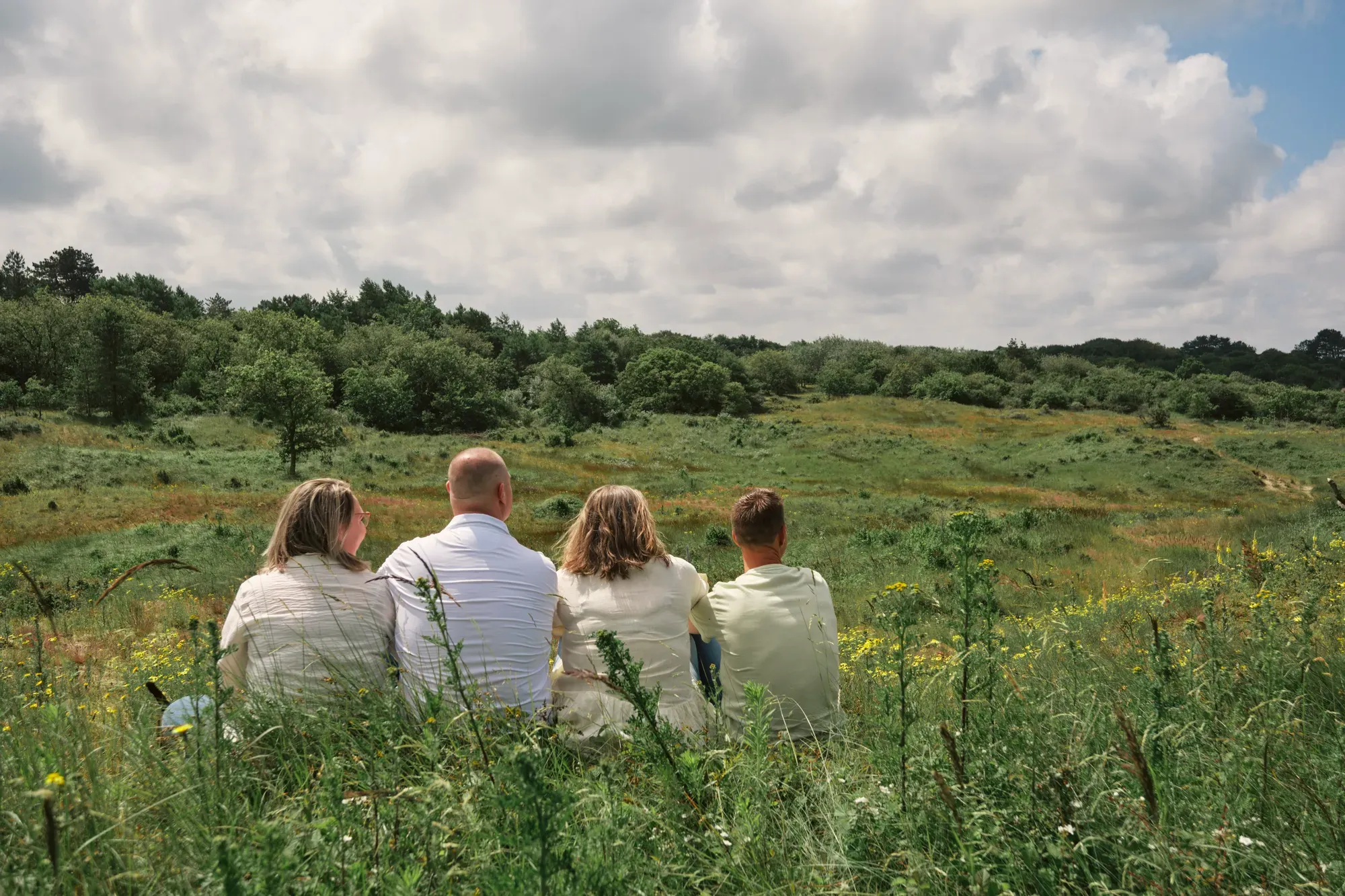 Vier mensen zitten van achteren gezien in het groen onder een bewolkte lucht