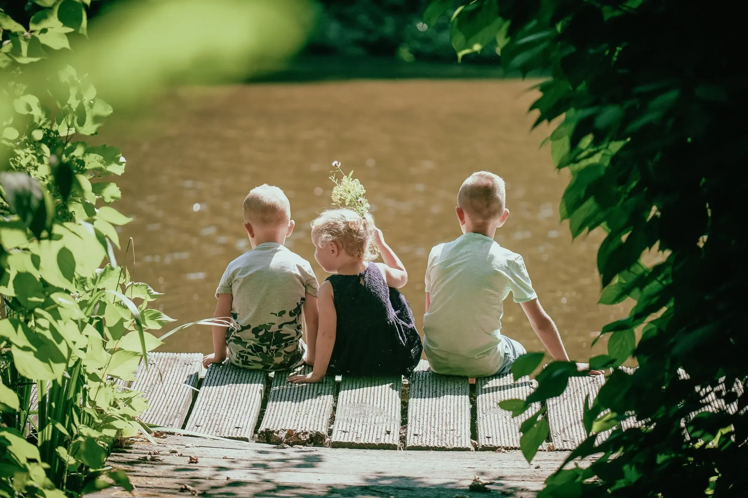 Drie kinderen zitten van achteren gezien aan het water