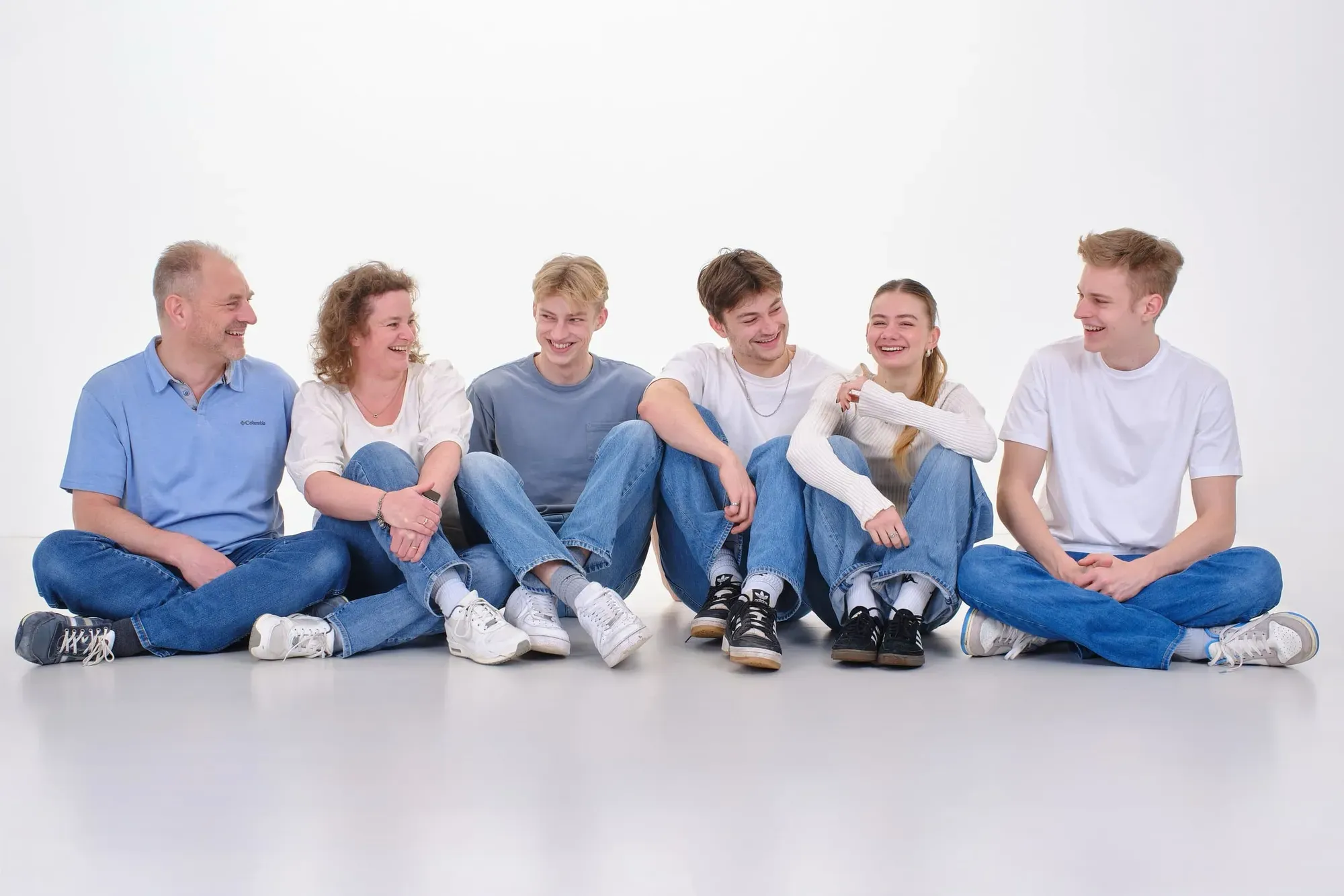 Familie in spijkerbroek en lichte shirts zit naast elkaar op de grond