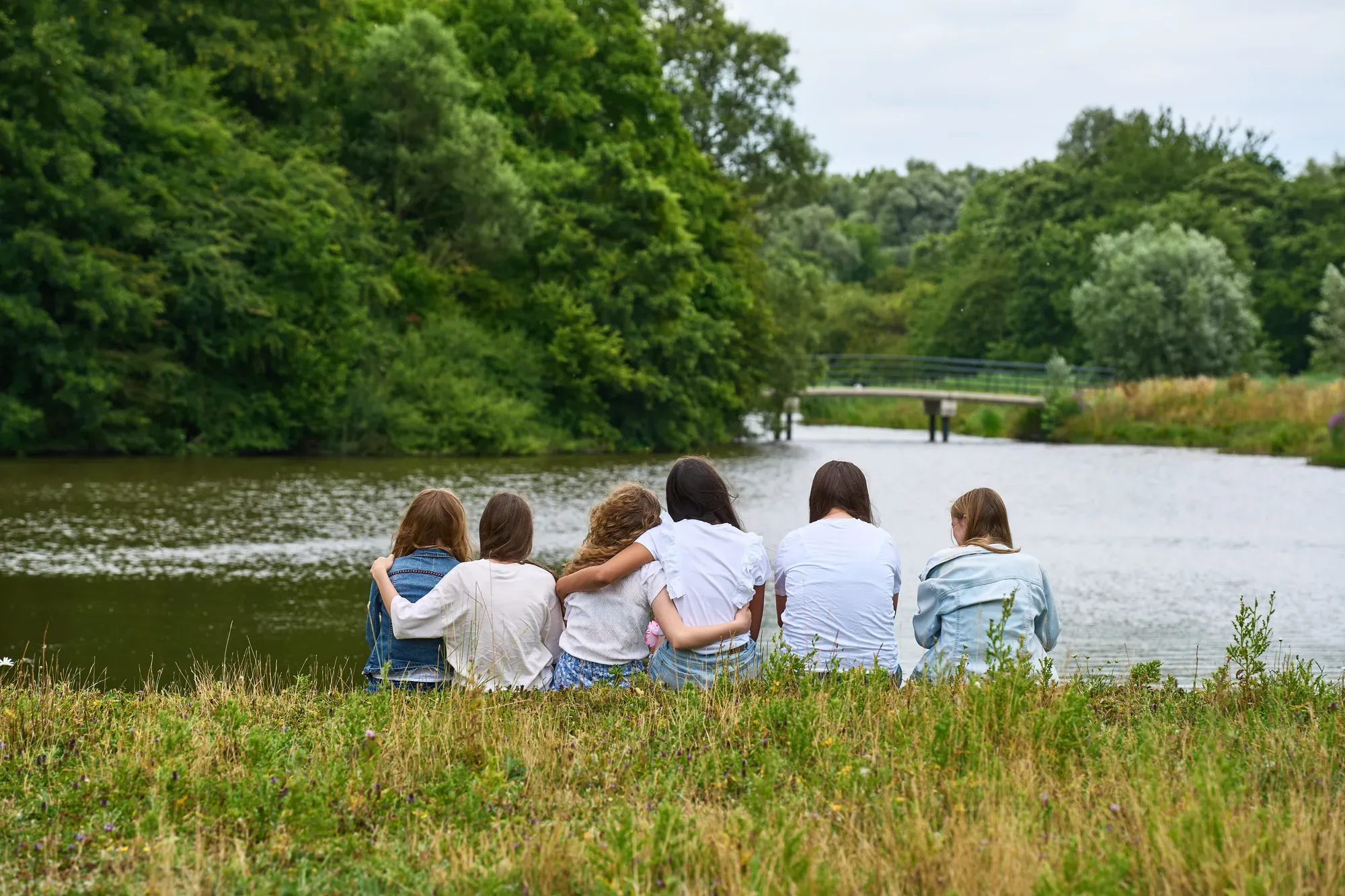 Zes jonge vrouwen zitten met de armen om elkaar heen aan het water in het Westerpark
