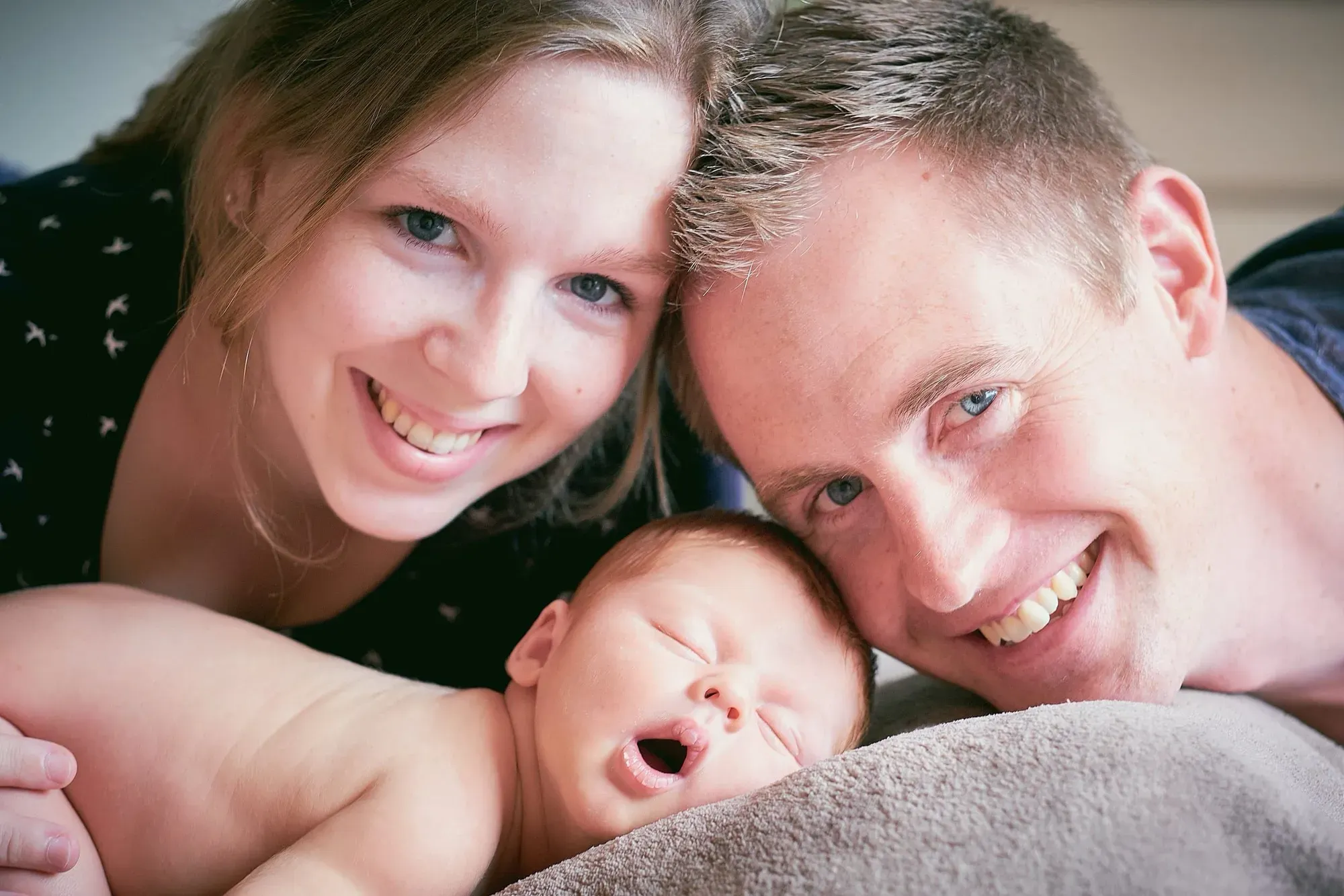 Ouders liggen samen bij hun baby en lachen