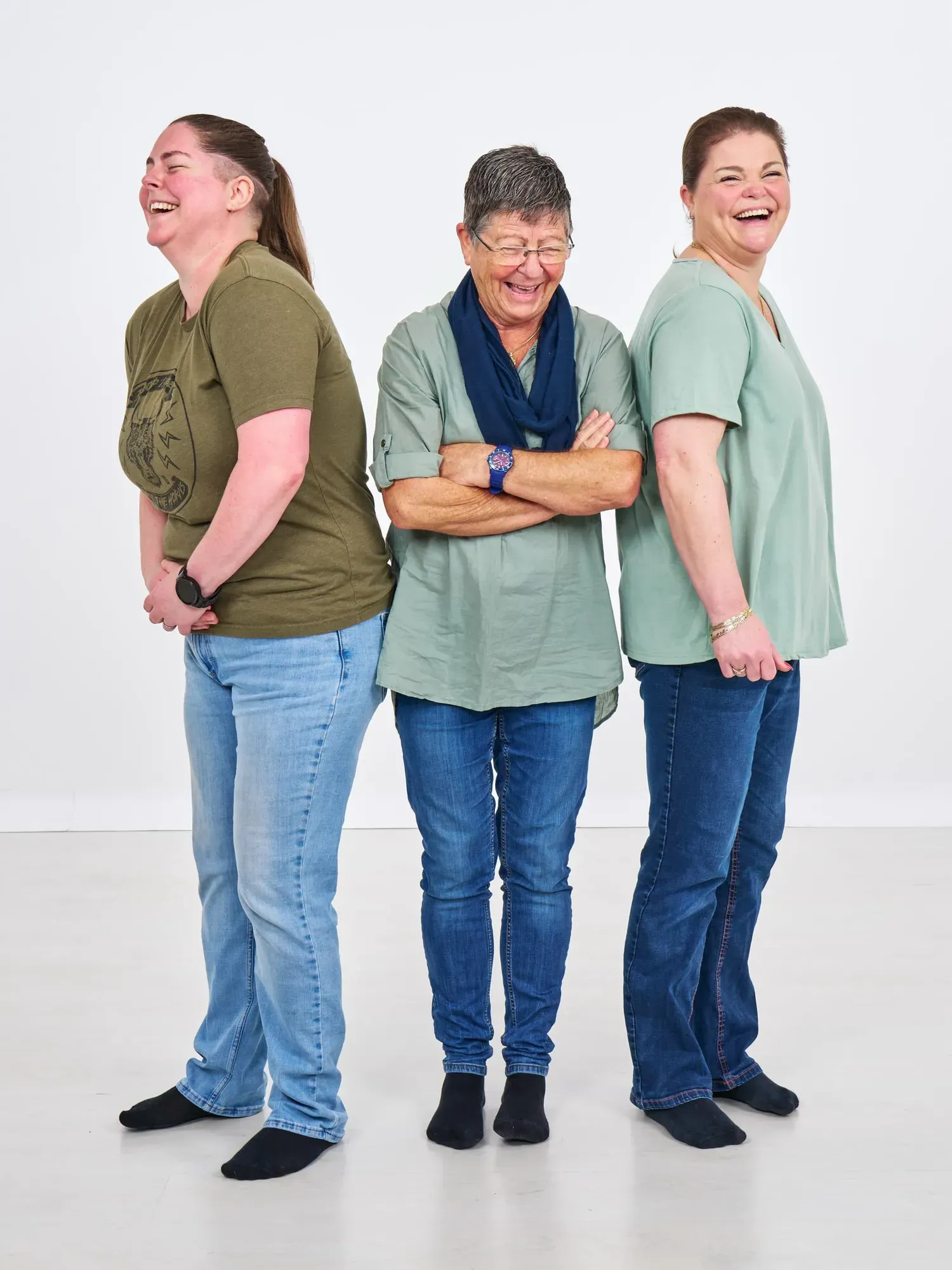 Drie vrouwen in spijkerbroek en groene shirts staan op sokken in de studio