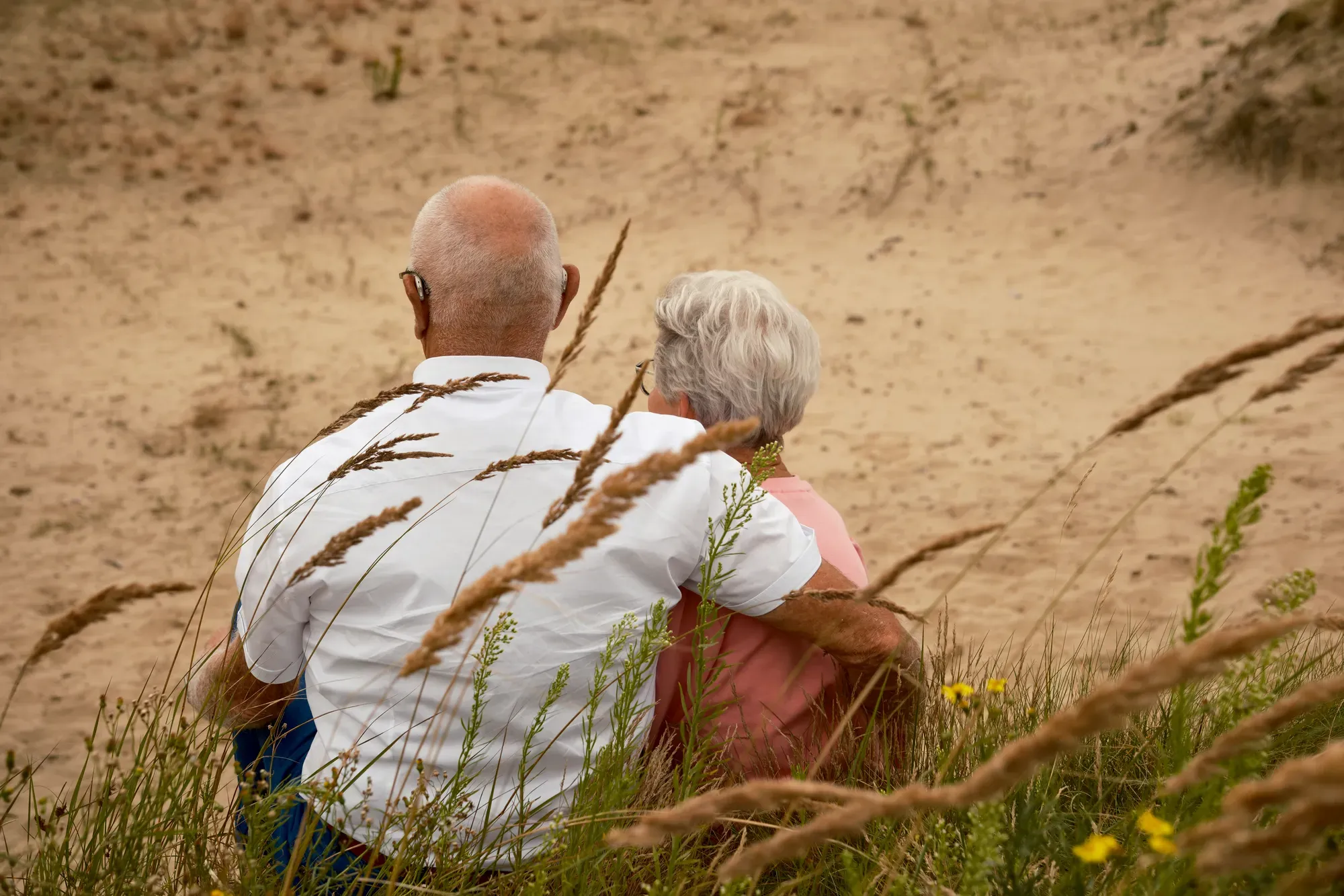 Ouder stel zit samen in het zand tussen het helmgras
